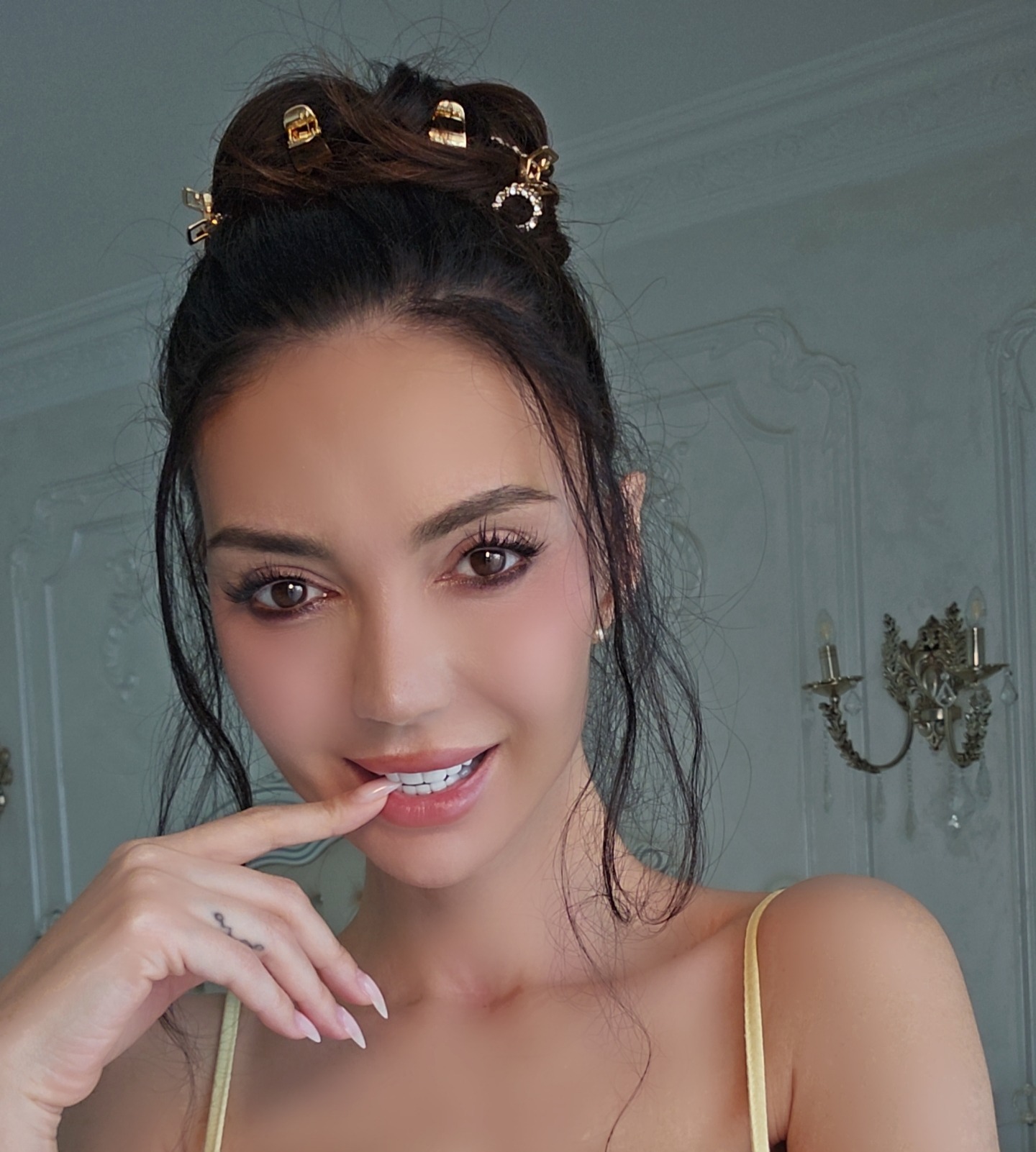 caylin posing with finger on lip wearing yellow spaghetti strap top in room