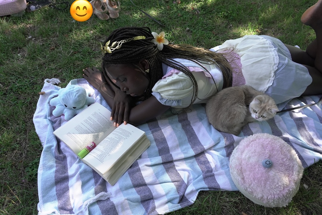 conymegan lying on a blanket reading a book wearing white and pink dress in park lawn