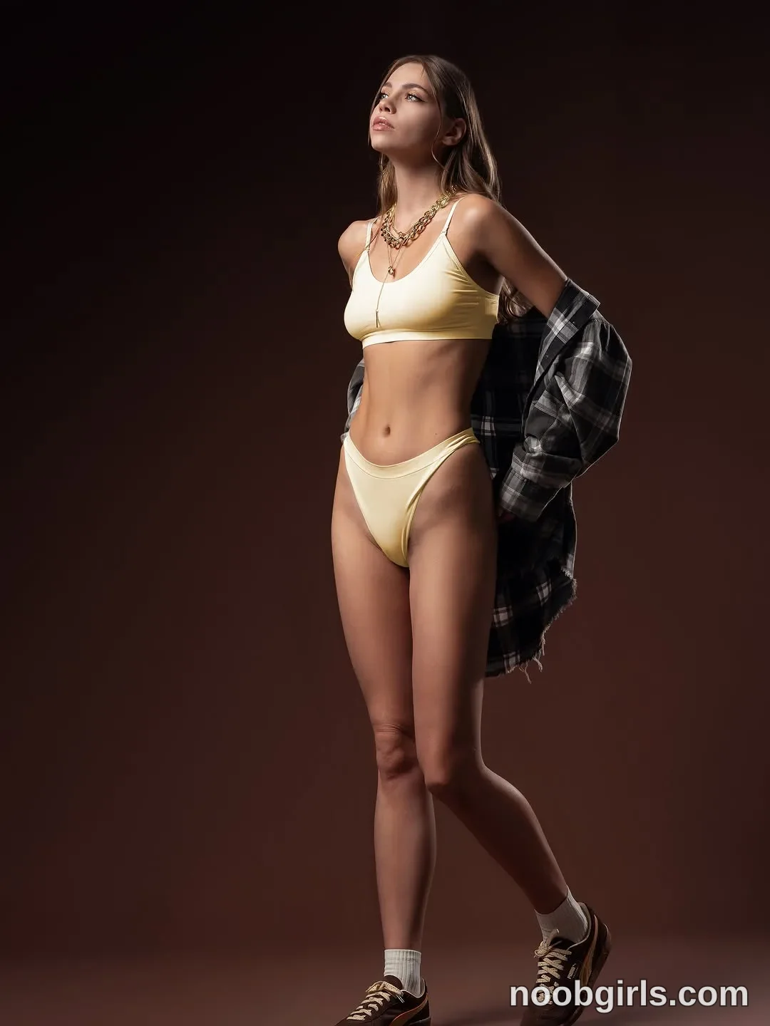 CoverM standing with one leg crossed behind the other wearing pale yellow cropped top with thin straps in photo studio