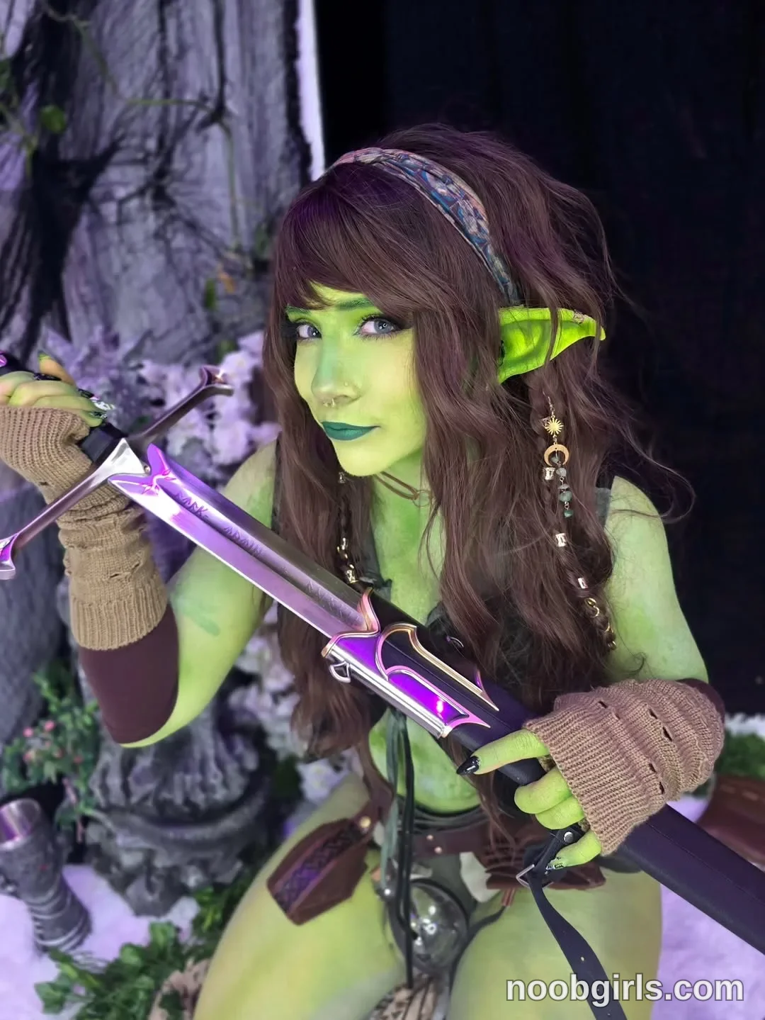Crimson Kitten Holding a sword diagonally across her body wearing Patterned multicoloured headband in staged area