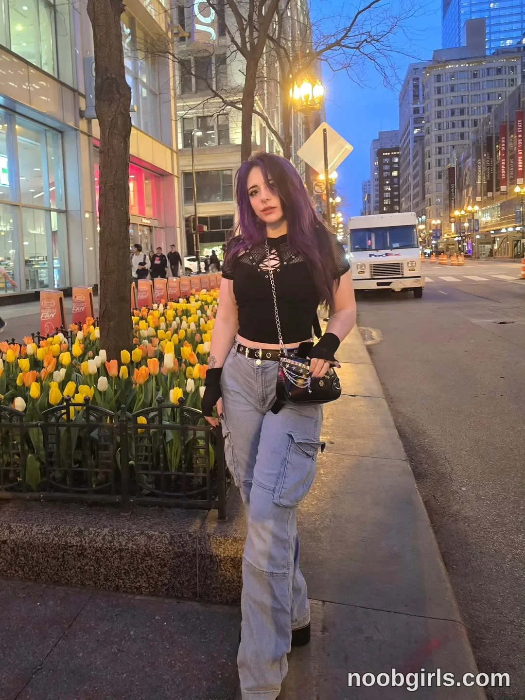 Crimson Kitten Standing on the sidewalk with one leg forward wearing Black short-sleeved cropped top with a lace-up neckline
