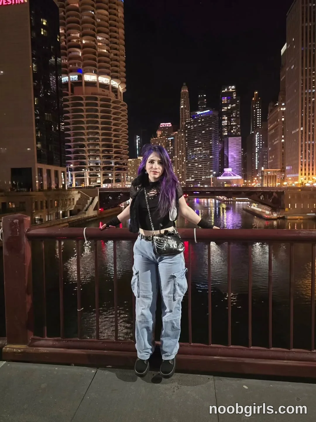 Crimson Kitten Standing facing the camera with her arms extended sideways wearing Black cropped top with a lace-up neckline