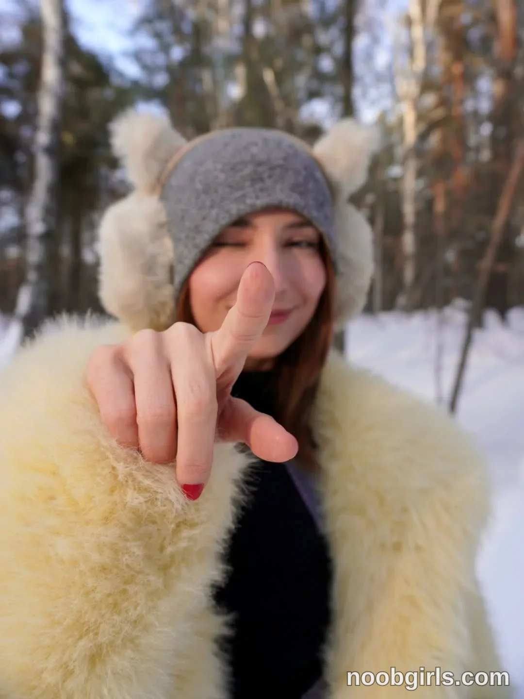 Maria extending one hand toward the camera wearing gray knit hat in snowy forest