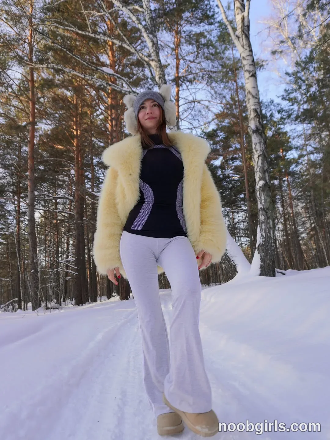 Maria standing or walking on the snowy path wearing gray knit hat with ear coverings in snowy forest path