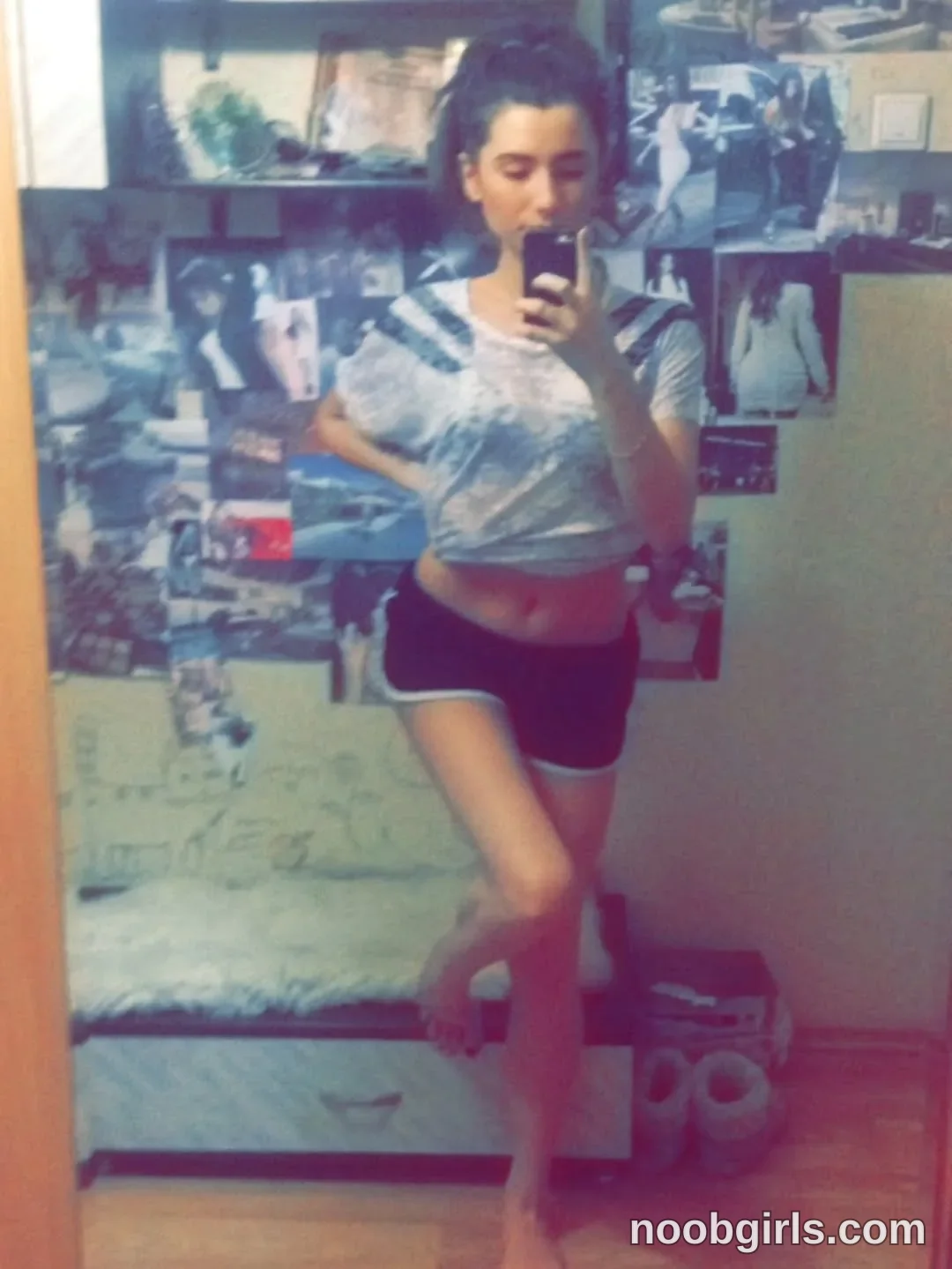 Maria Taking a mirror photograph with a smartphone wearing gray-and-white patterned short-sleeve top in bedroom