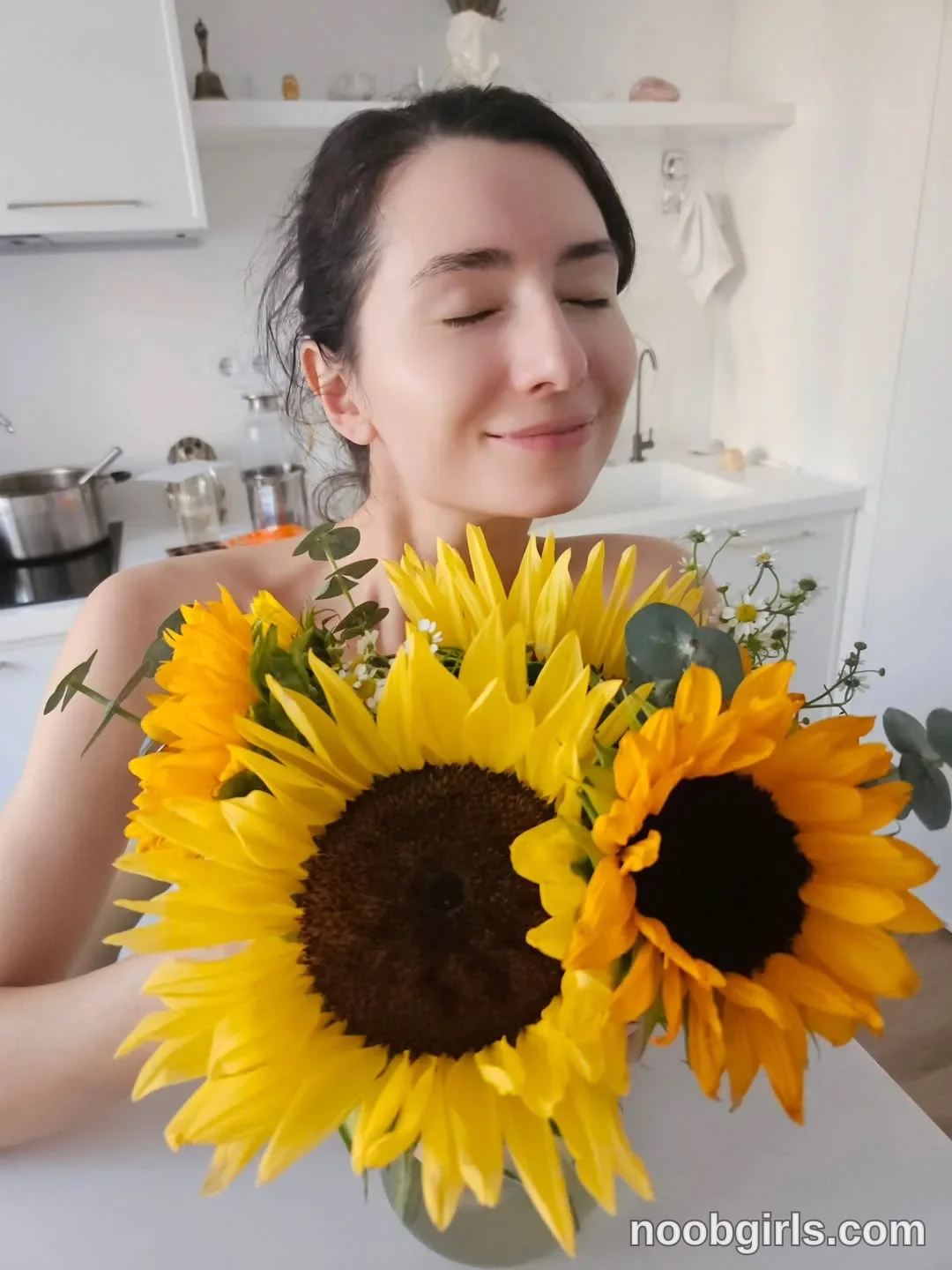 Maria Holding a bouquet of flowers in front of her wearing light-colored sleeveless garment, partly obscured by flowers
