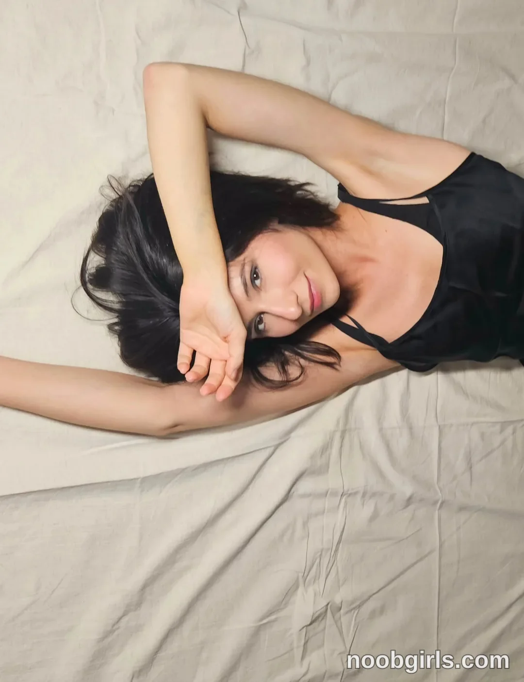 crystalnut lying on back with arm raised wearing black camisole in bed