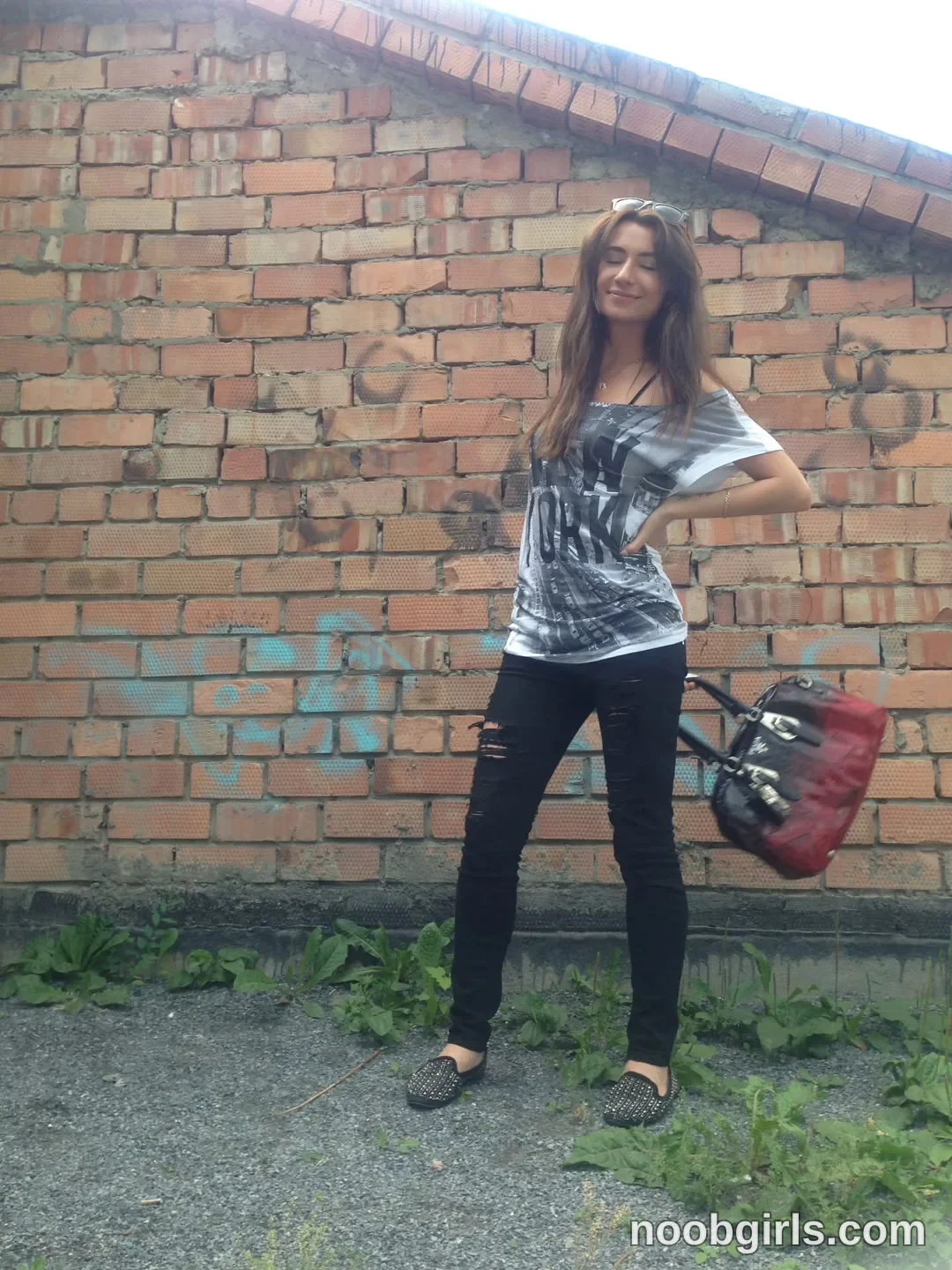 crystalnut posing with a handbag wearing grey graphic t-shirt in front of a brick wall