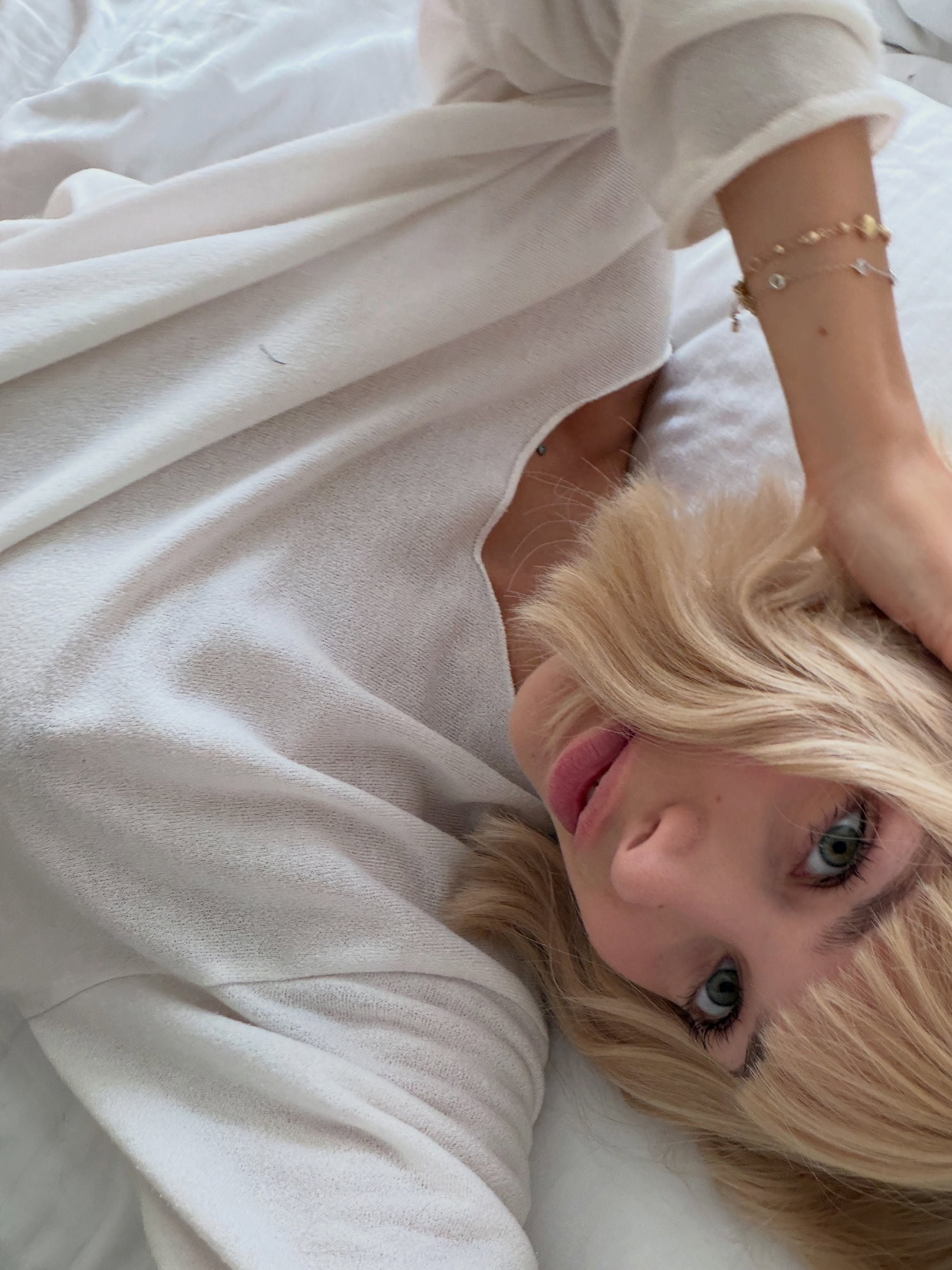 cutieeeeva lying down wearing white long-sleeved top in bed