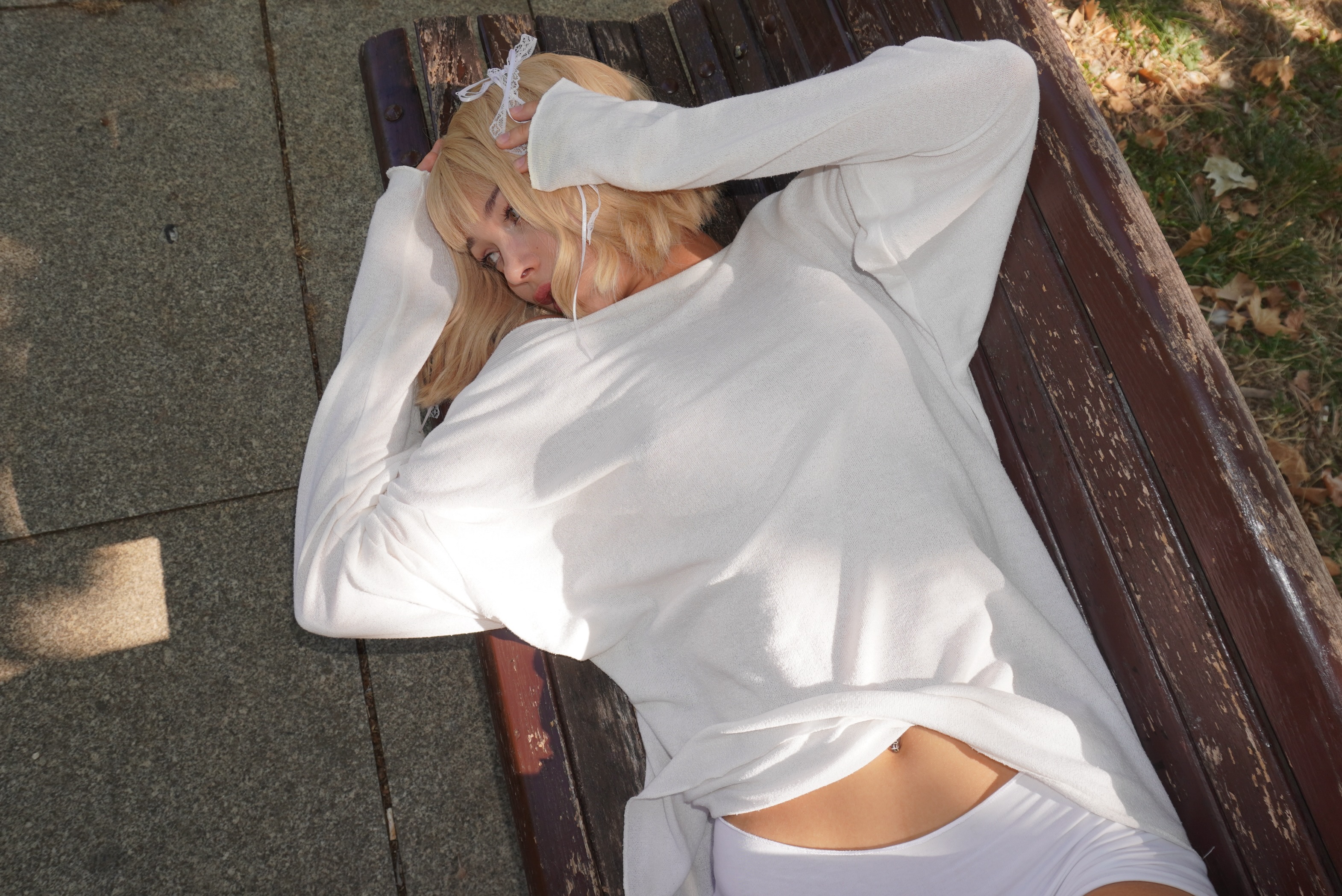 cutieeeeva lying on a wooden bench wearing white long-sleeved top in park bench