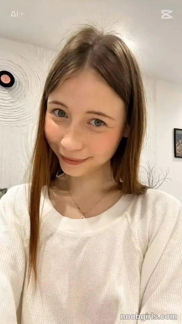 DELORA facing the camera with her head tilted slightly wearing white long-sleeved knit top in residential room