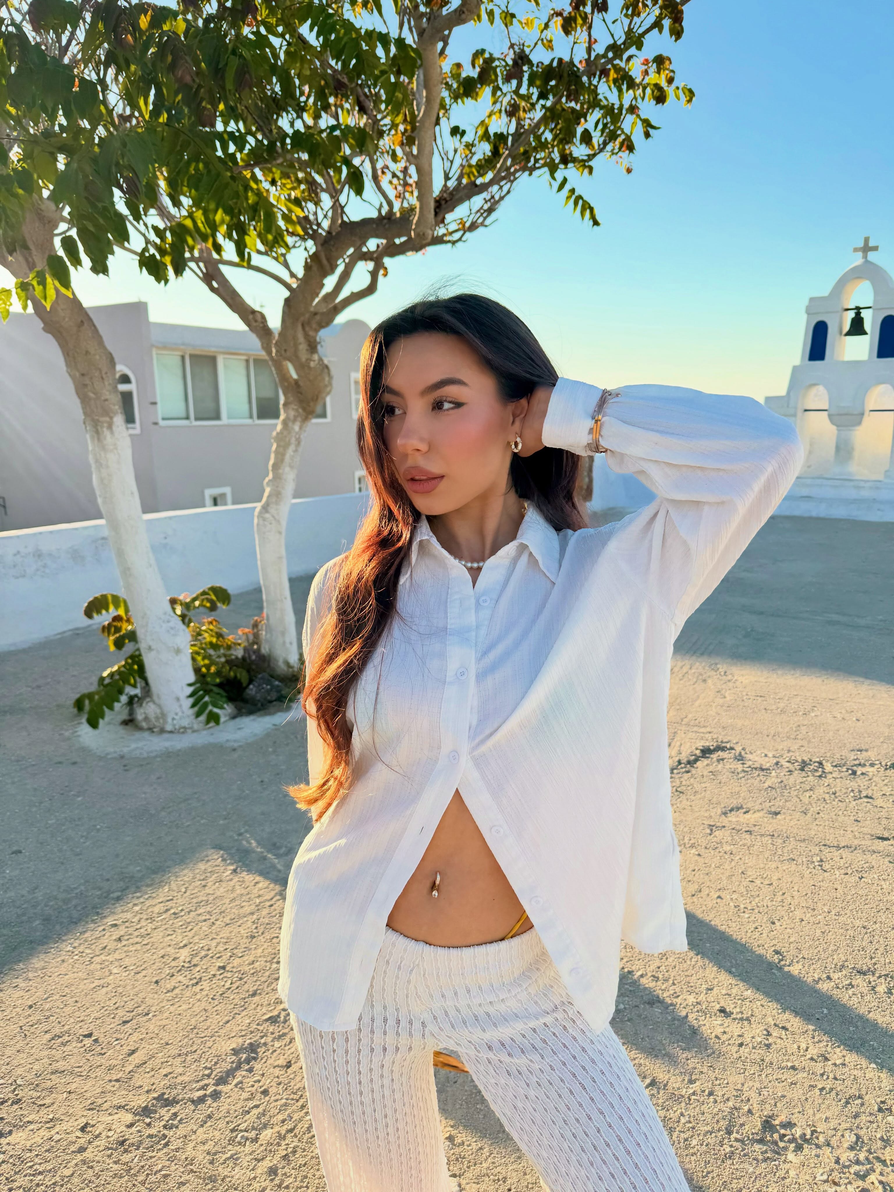 deniseglows posing with hand behind head wearing white button-up shirt in courtyard