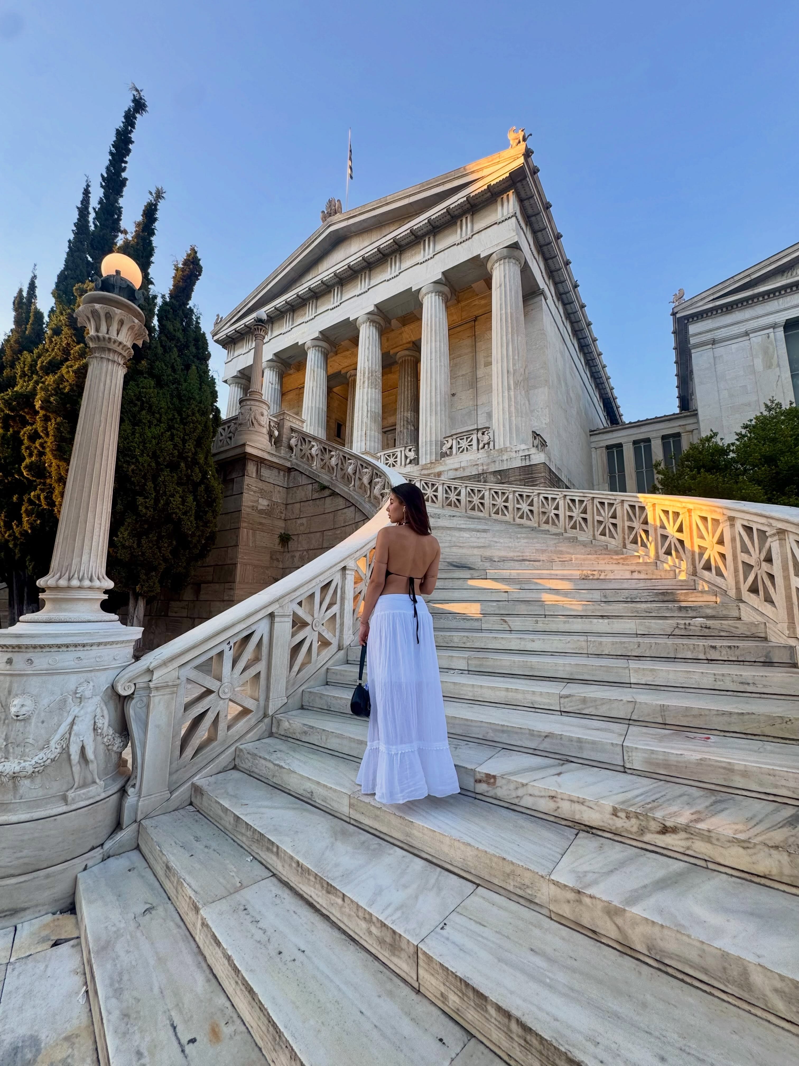 deniseglows standing on stairs wearing black backless top in marble staircase outside neoclassical building