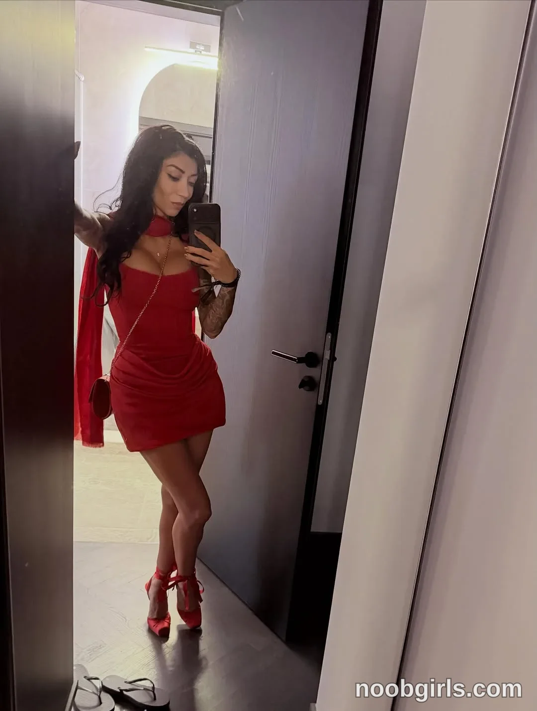 Evelyne Standing with her legs crossed wearing Red fitted sleeveless mini dress in doorway beside a bathroom