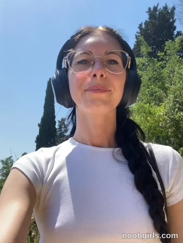 Nikki Gia Facing the camera with one arm extended toward it wearing Light grey short-sleeved crew-neck top in area
