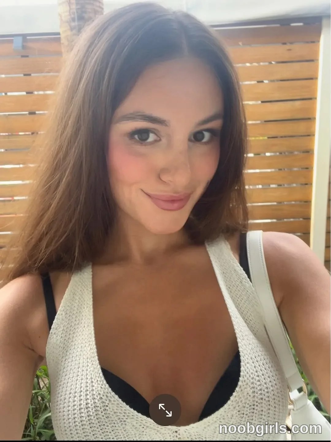 Gracie Smith facing the camera with one arm extended toward it wearing cream open-knit sleeveless top with a low neckline