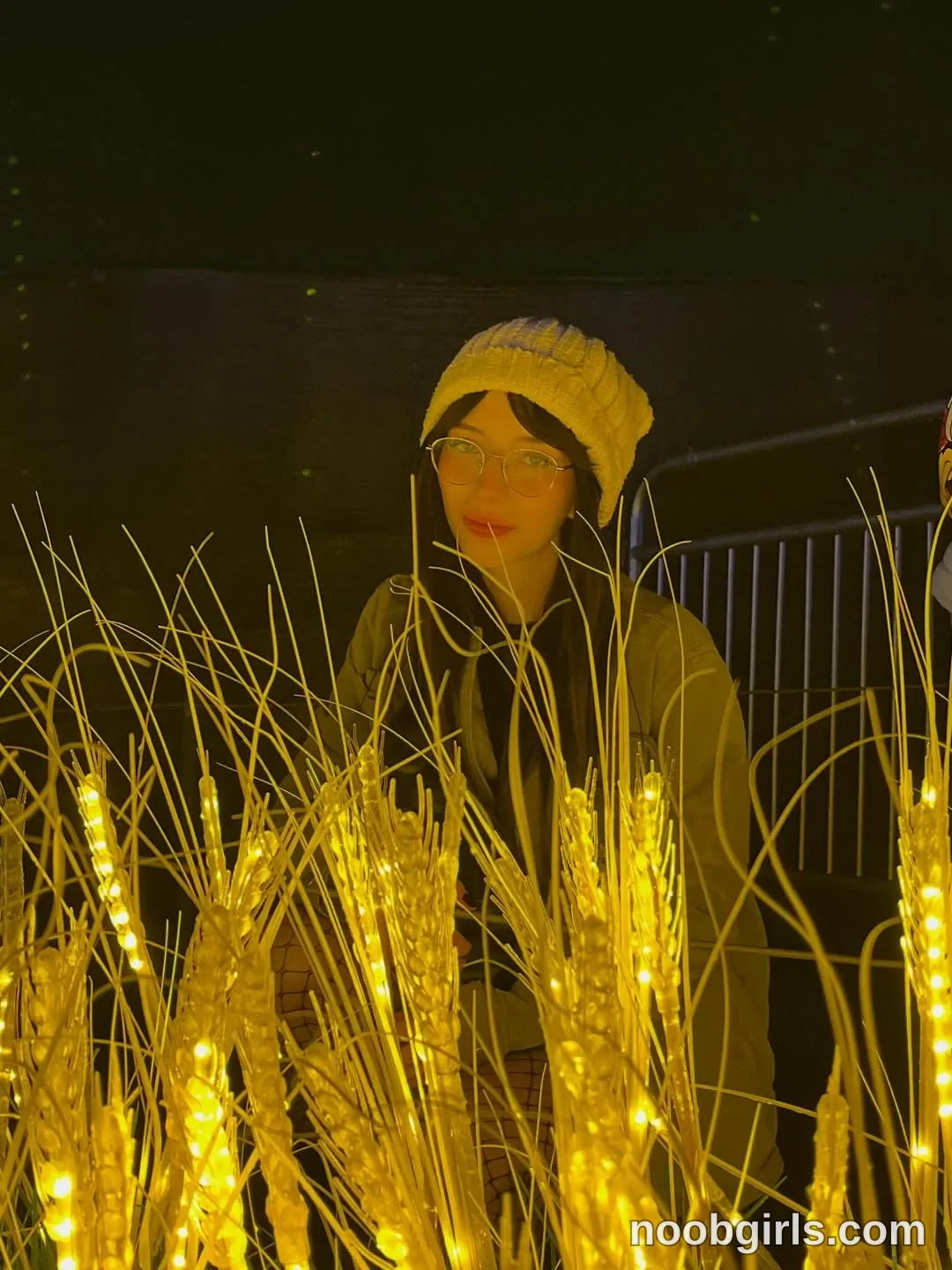 Jelly Standing behind the illuminated stems with her head turned slightly to the left of the frame