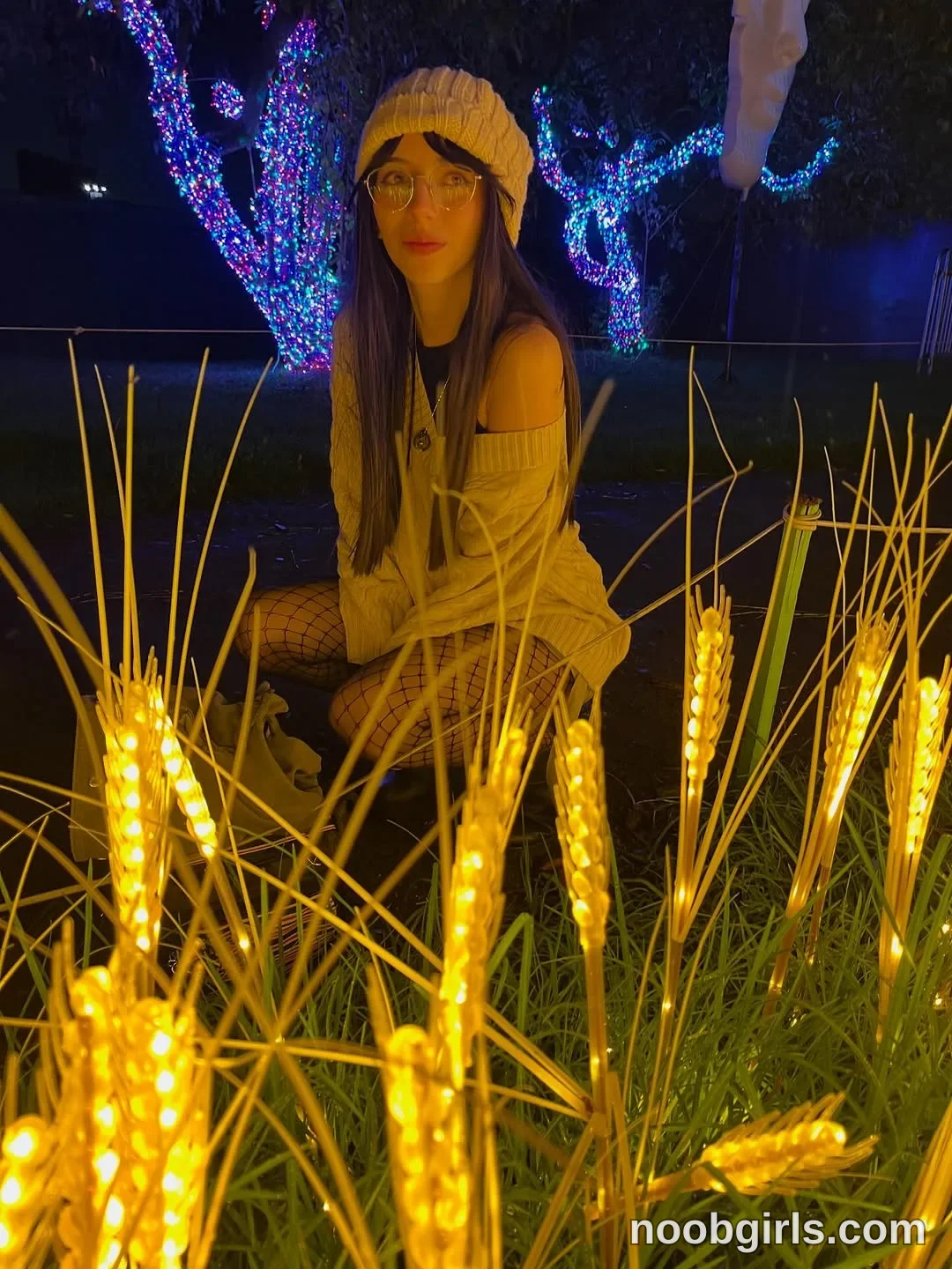 Jelly Crouching among the light decorations with her knees bent wearing Cream knitted beanie in grassy area