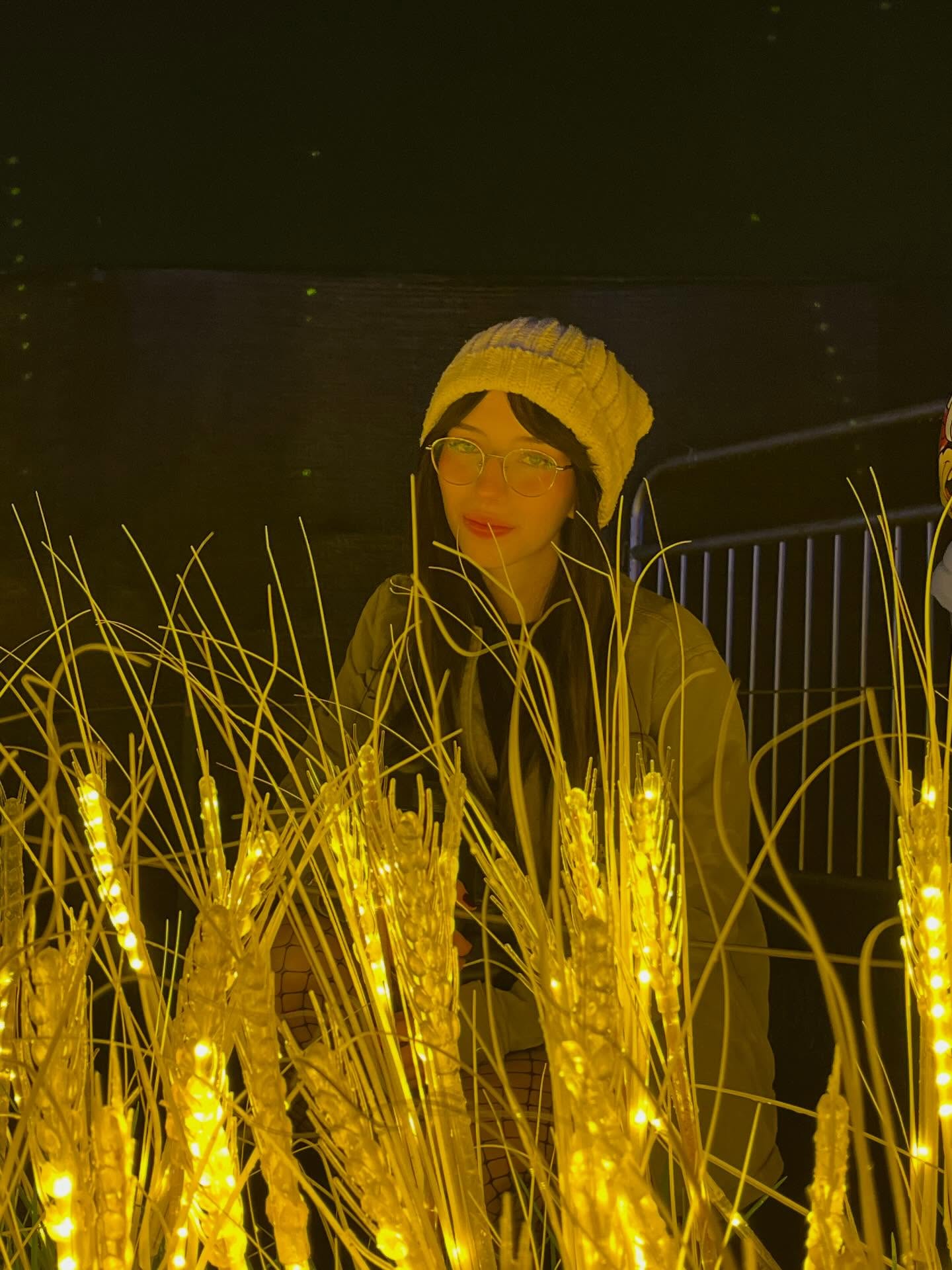 Jelly Standing behind the illuminated stalks with her head turned slightly toward the left side of the frame