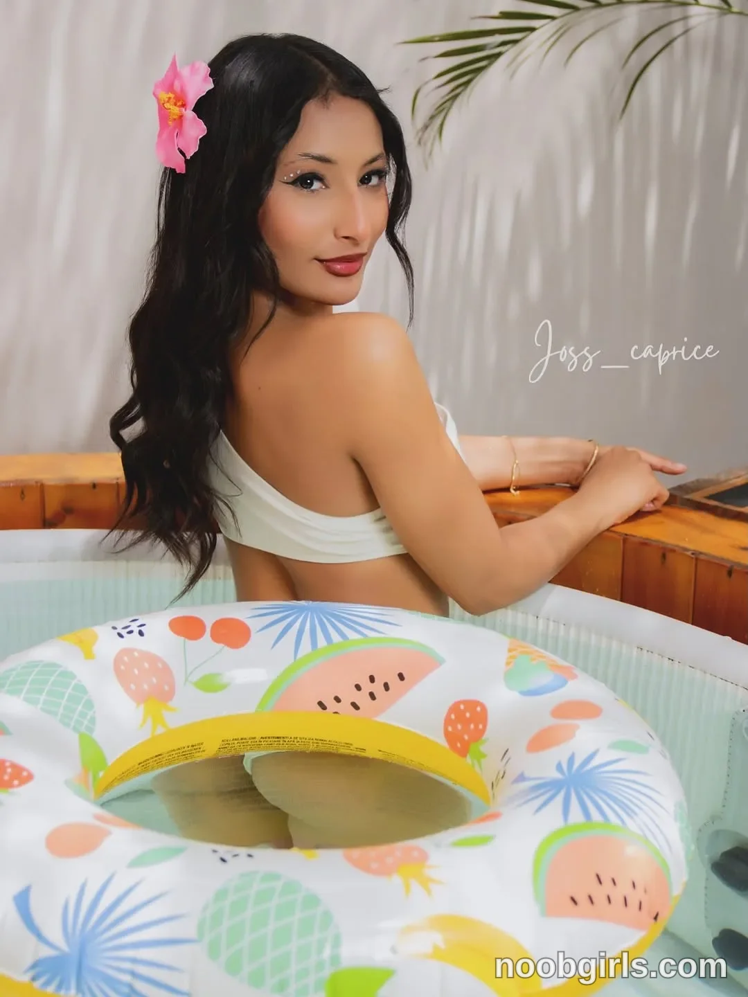 Joss sitting or kneeling in water inside a tub wearing white one-shoulder bikini top in or covered space