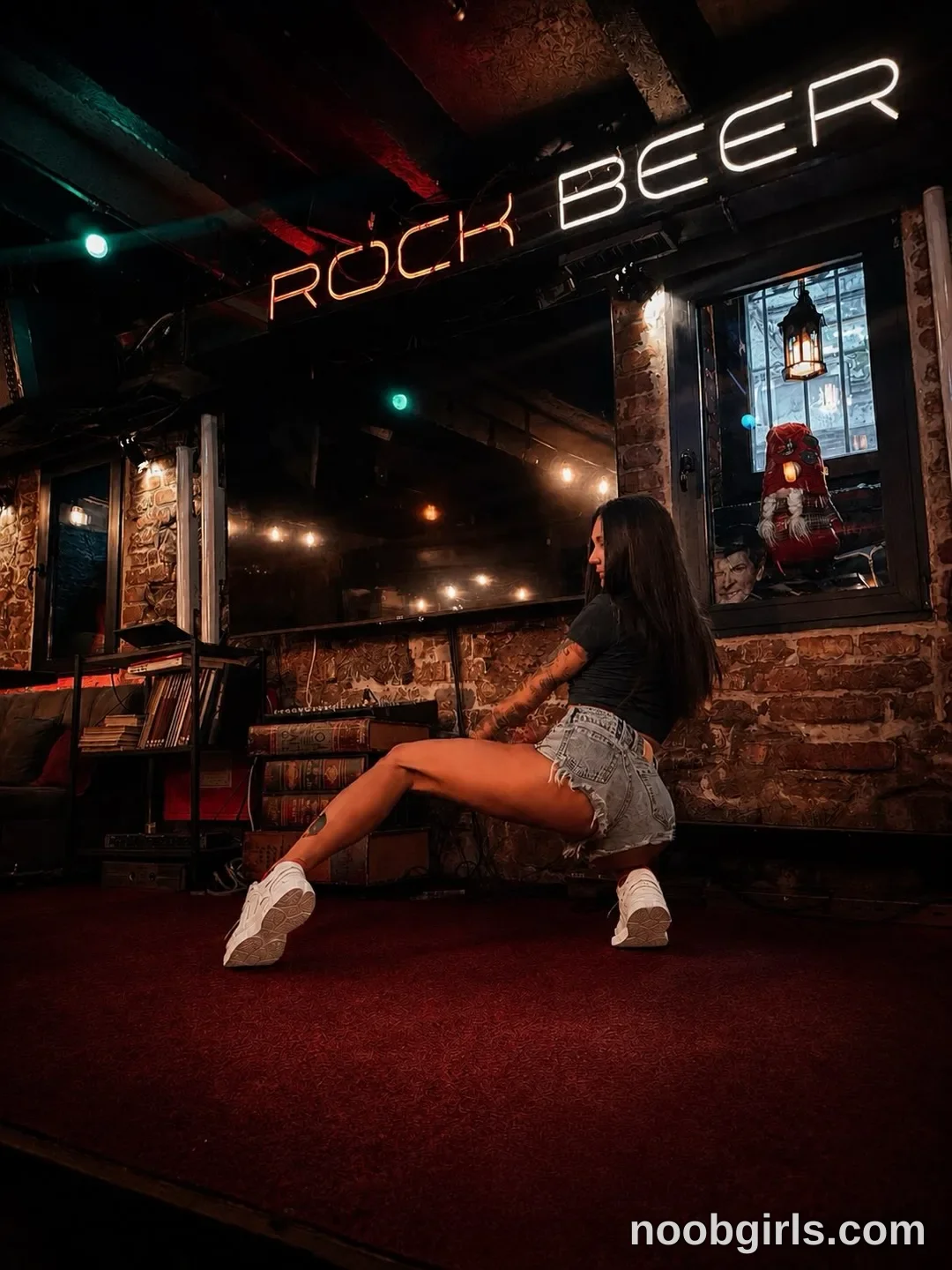 Alice crouching low with her knees bent wearing Black short-sleeved top in bar