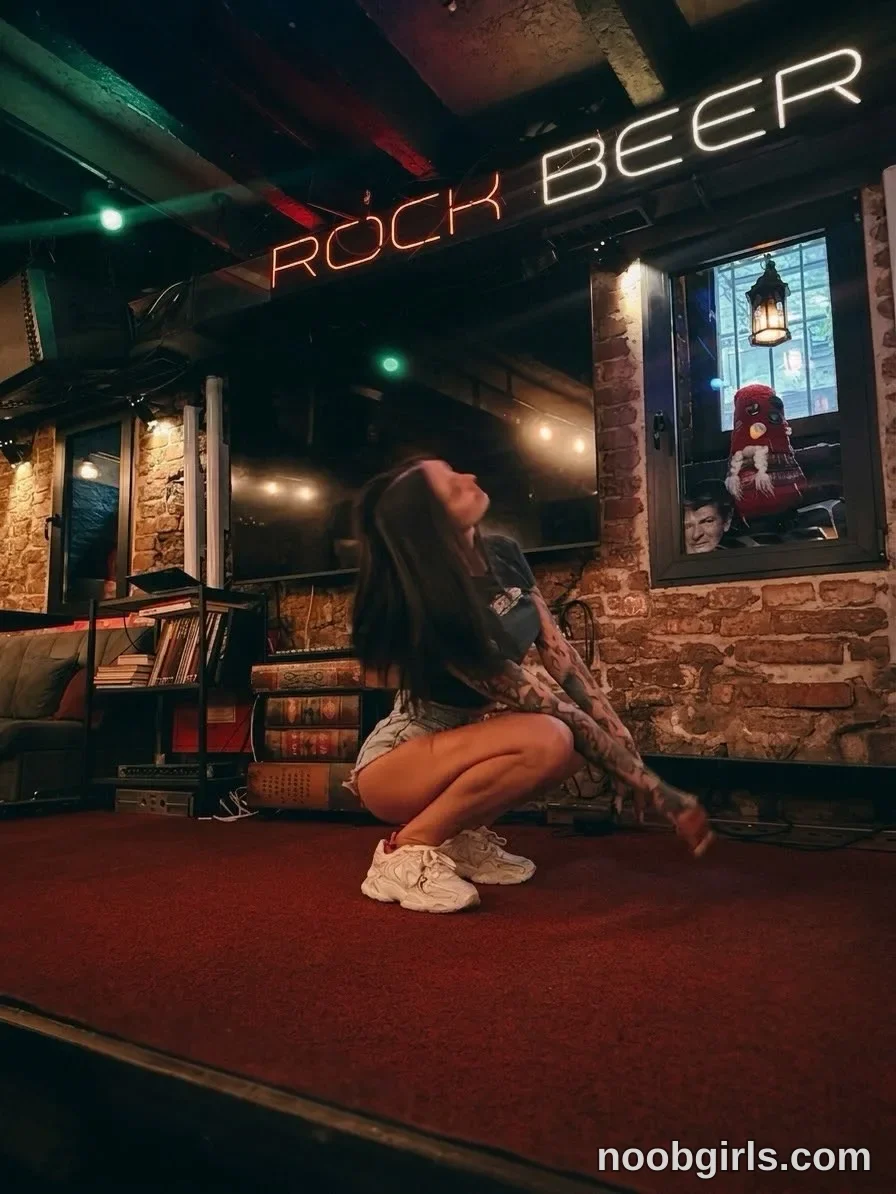 Alice crouching with her knees bent wearing Dark short-sleeved T-shirt with a light-coloured graphic in bar