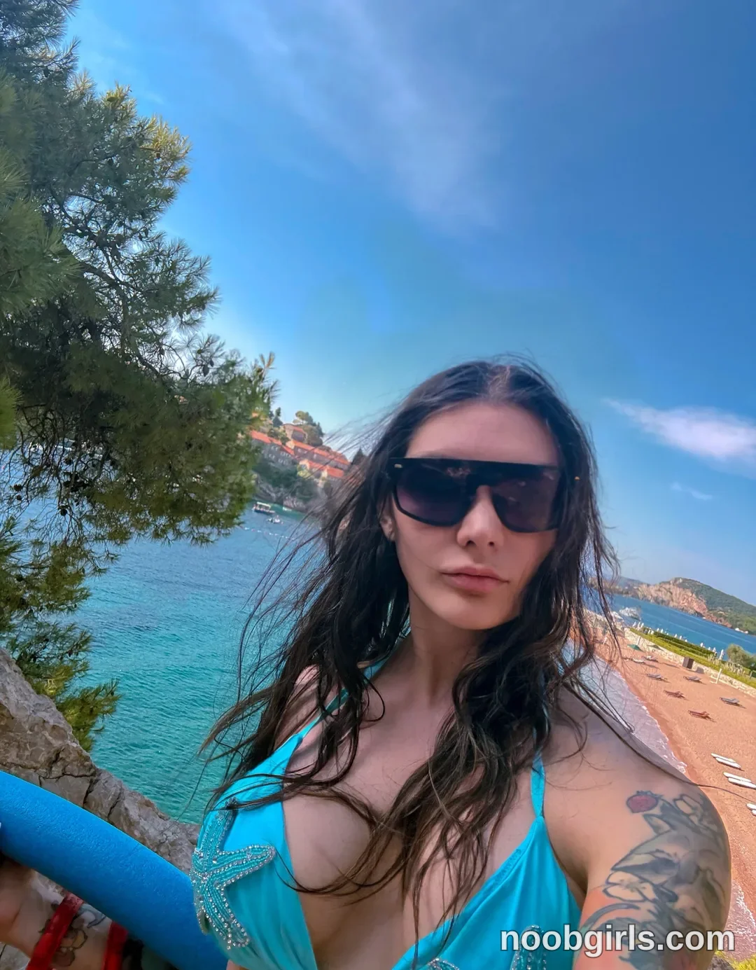 Alice Holding the railing with one hand wearing Turquoise bikini top with silver-coloured decorative trim
