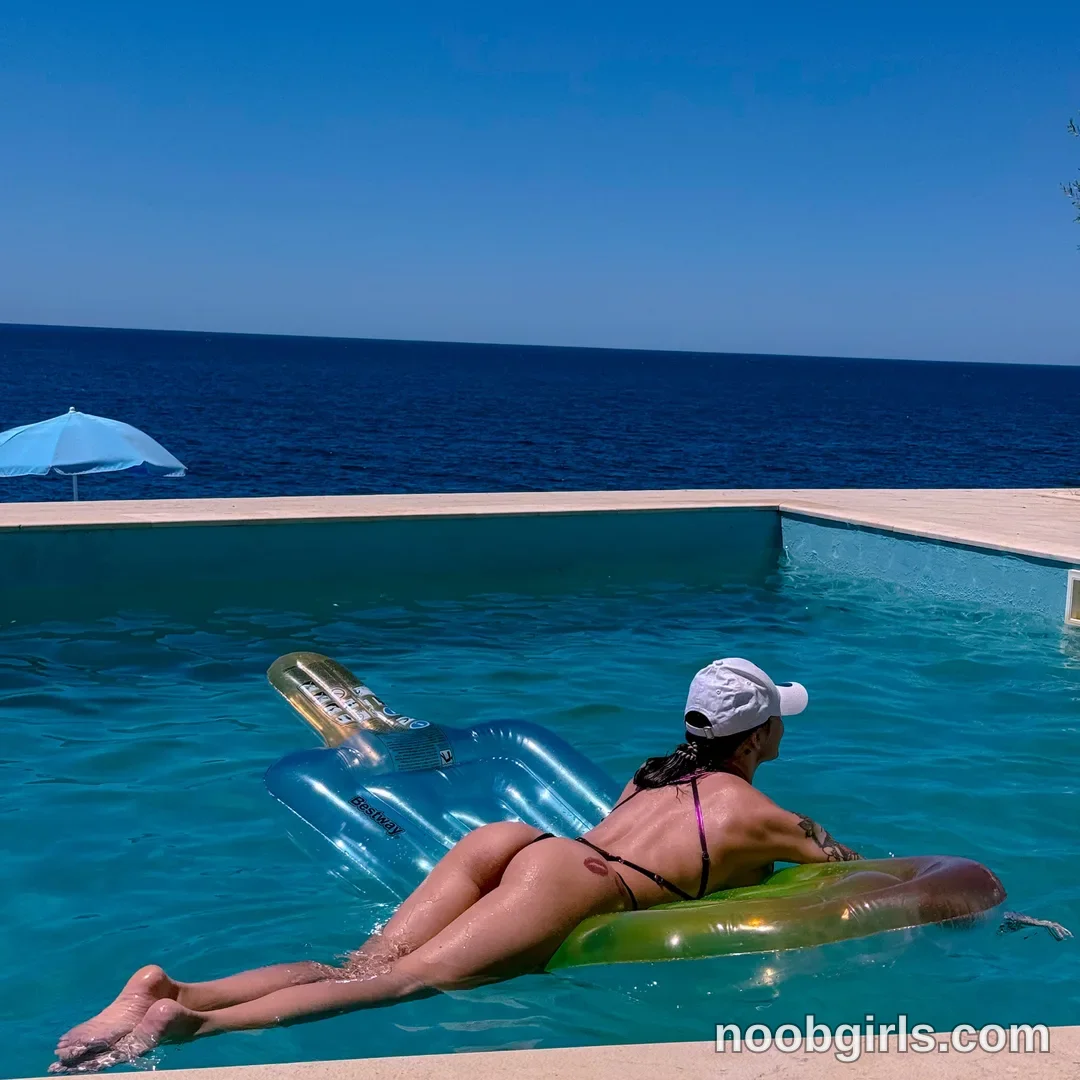 Alice lying face down on an inflatable lounger in the pool wearing purple string bikini in swimming pool overlooking the sea