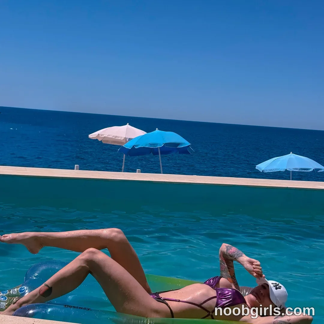 Alice Reclining on an inflatable lounger in the pool with her legs bent wearing Purple bikini with dark trim and straps