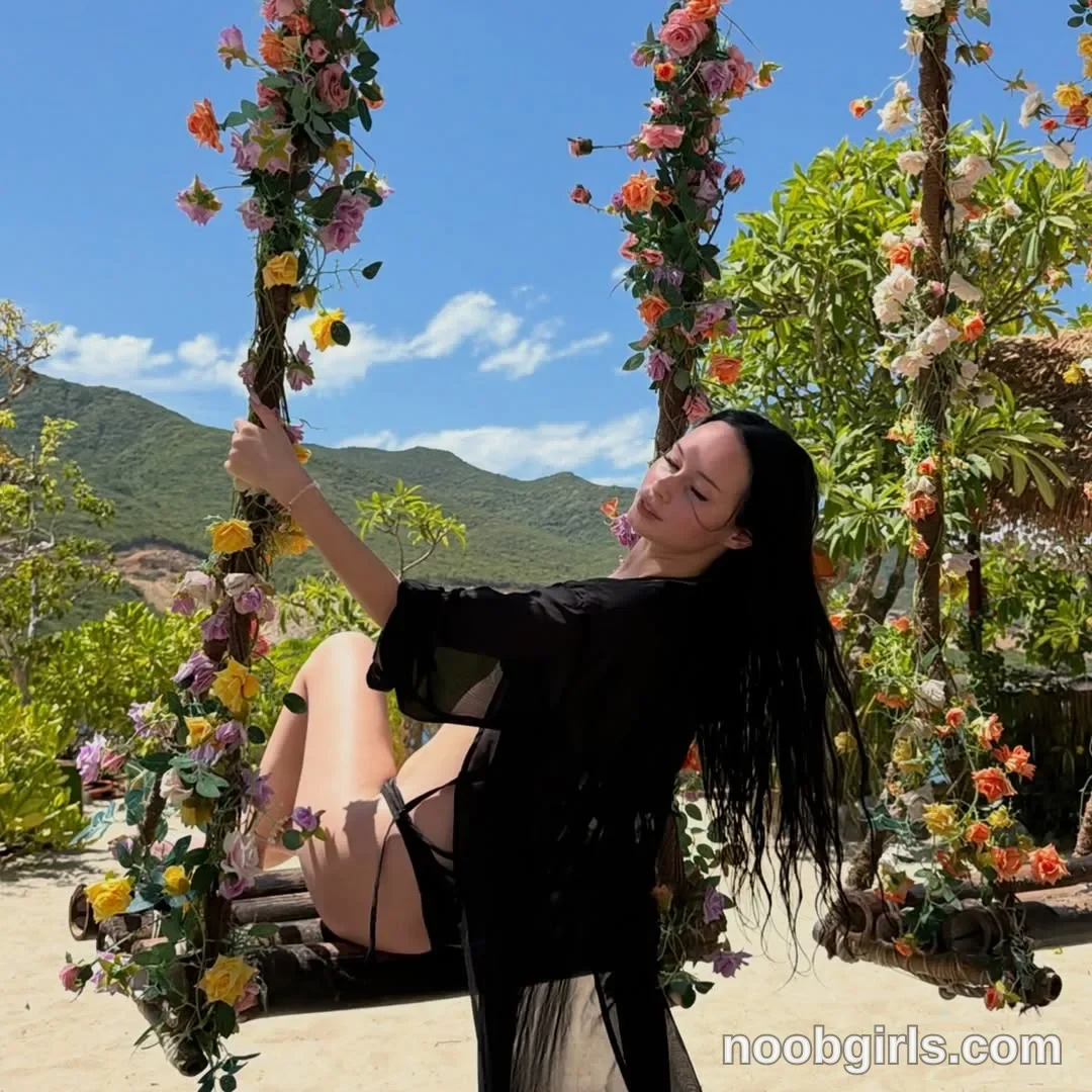 Megan Sitting sideways on a swing with bent knees wearing Black bikini bottoms with side ties in garden area