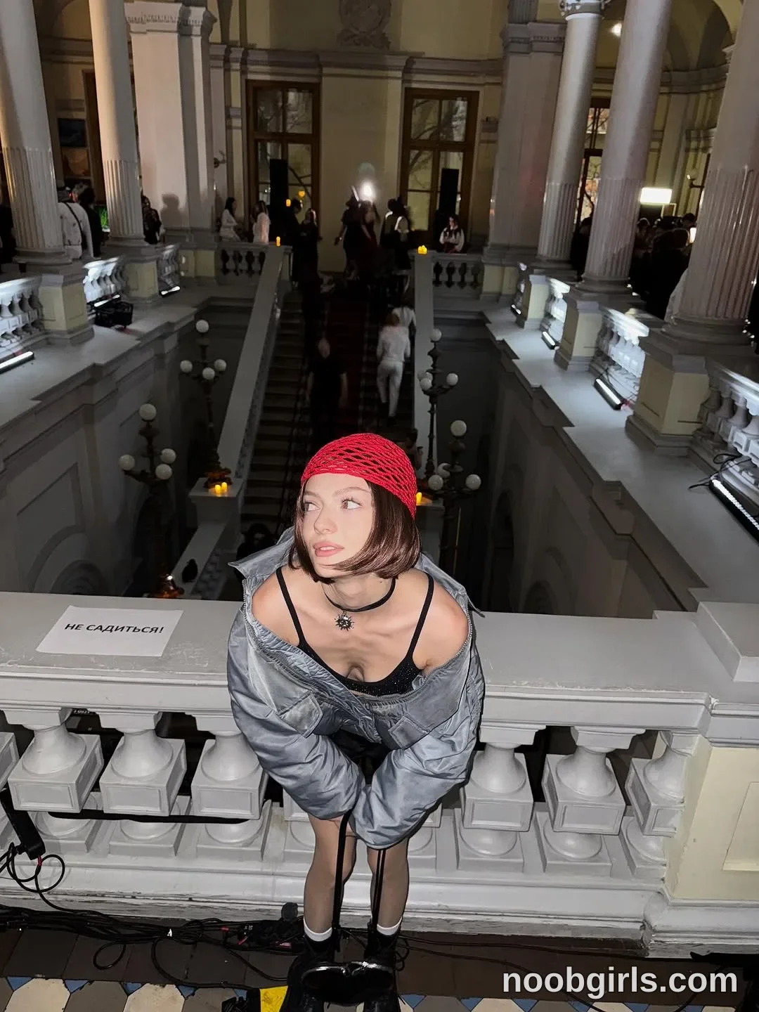 Milly Leaning forward with her hands together in front of her legs wearing Red crocheted cap in a large hall
