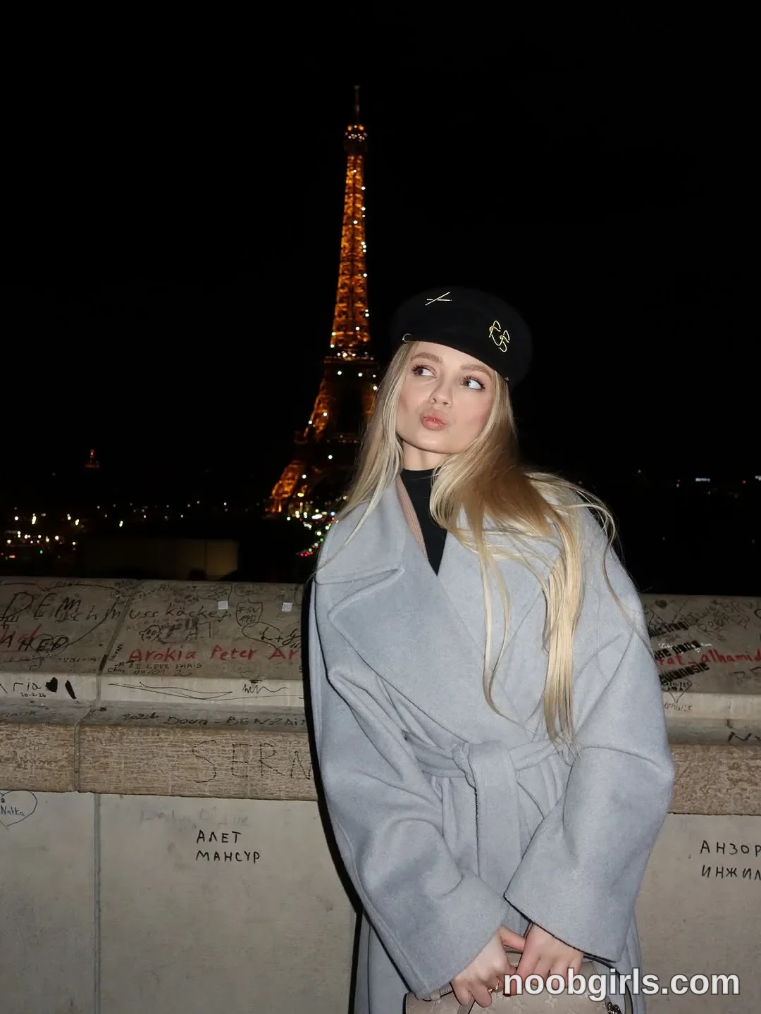 Nastya Standing with her hands together in front of her wearing Light grey belted coat with wide lapels