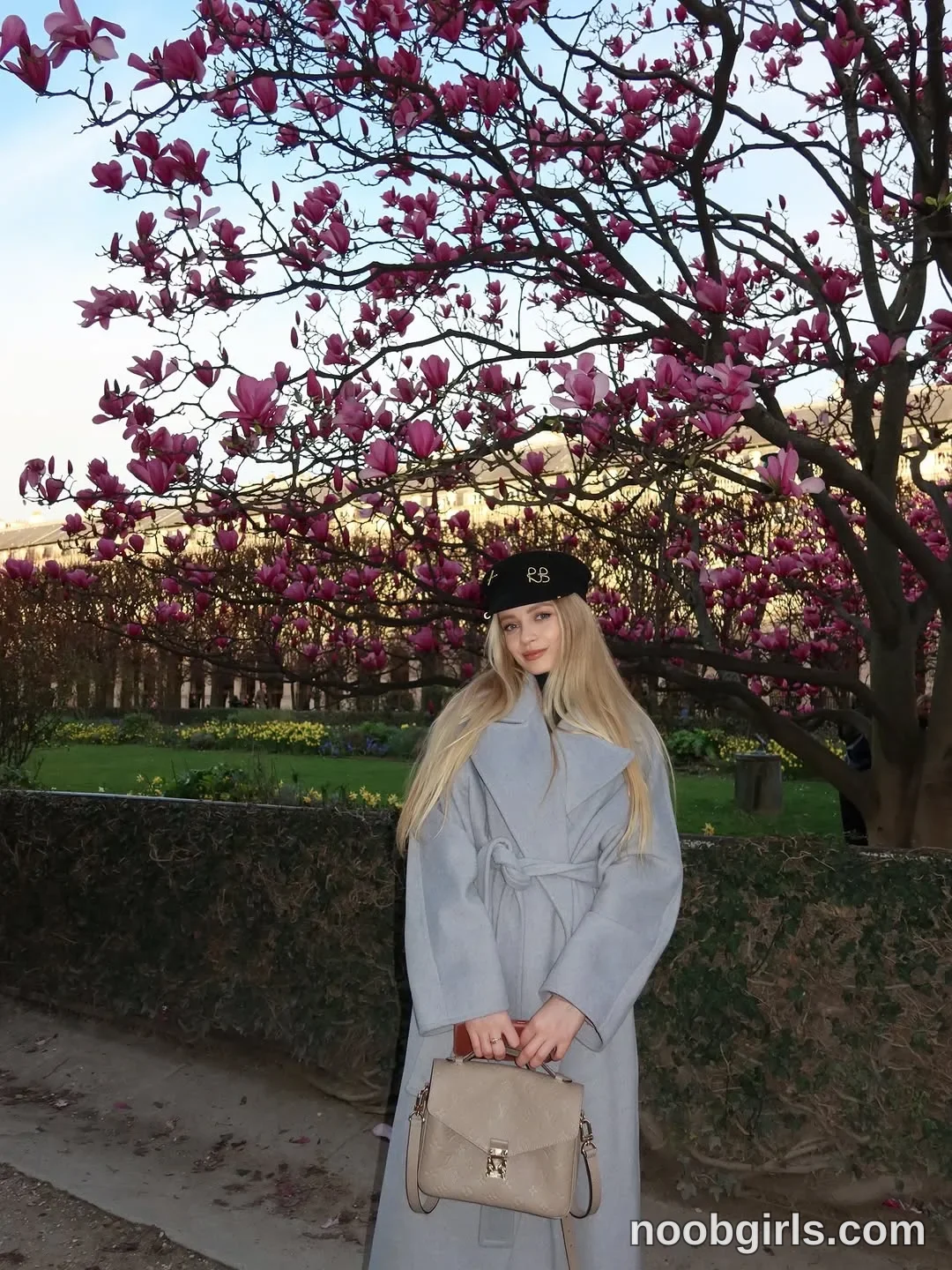 Nastya Standing on the path wearing Light grey long coat with wide lapels and a tied waist belt in garden