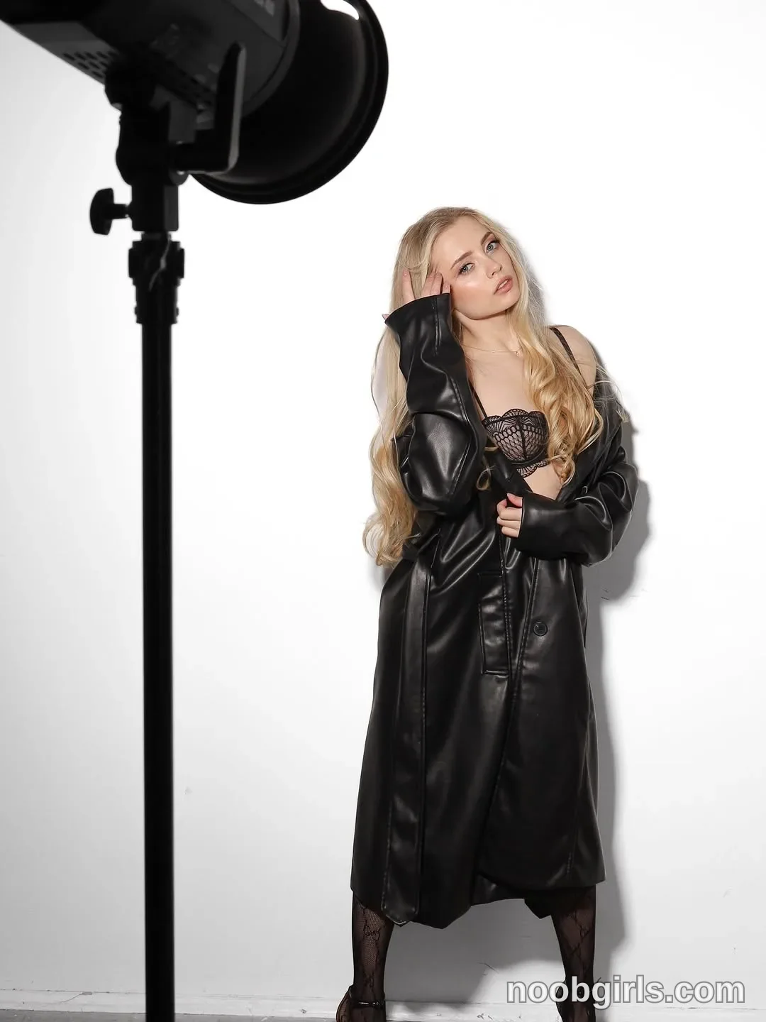 Nastya Standing with her head tilted wearing Long black leather-look coat in photography studio