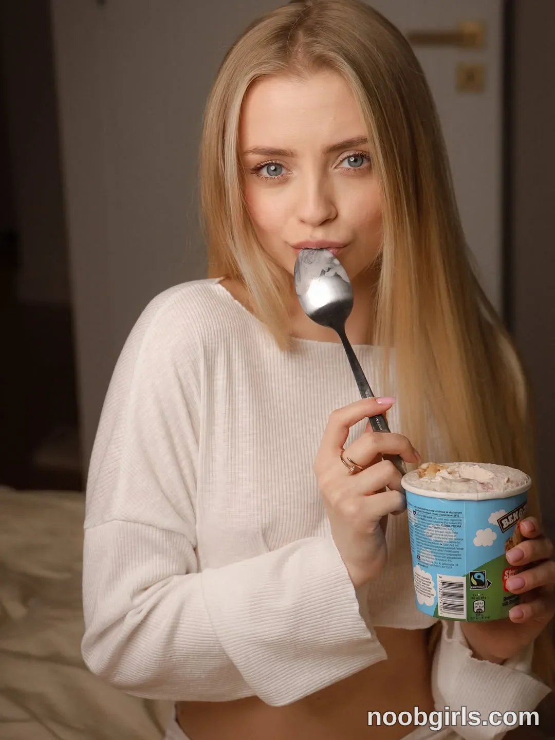 Nastya Holding a spoon against her lips with one hand wearing White ribbed long-sleeved cropped top in room