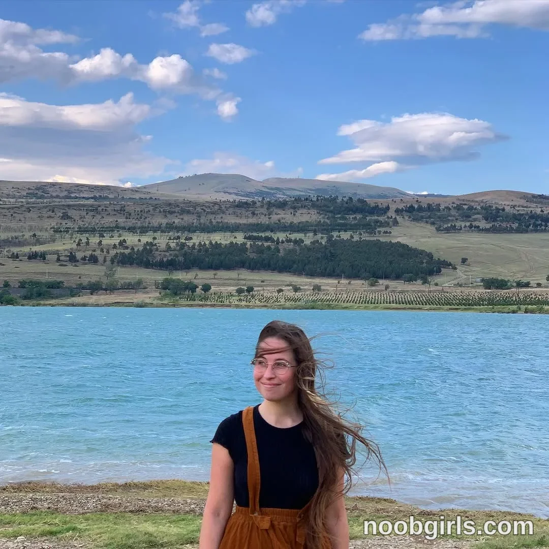 Riley Standing beside the water with her arms lowered wearing Black short-sleeved shirt