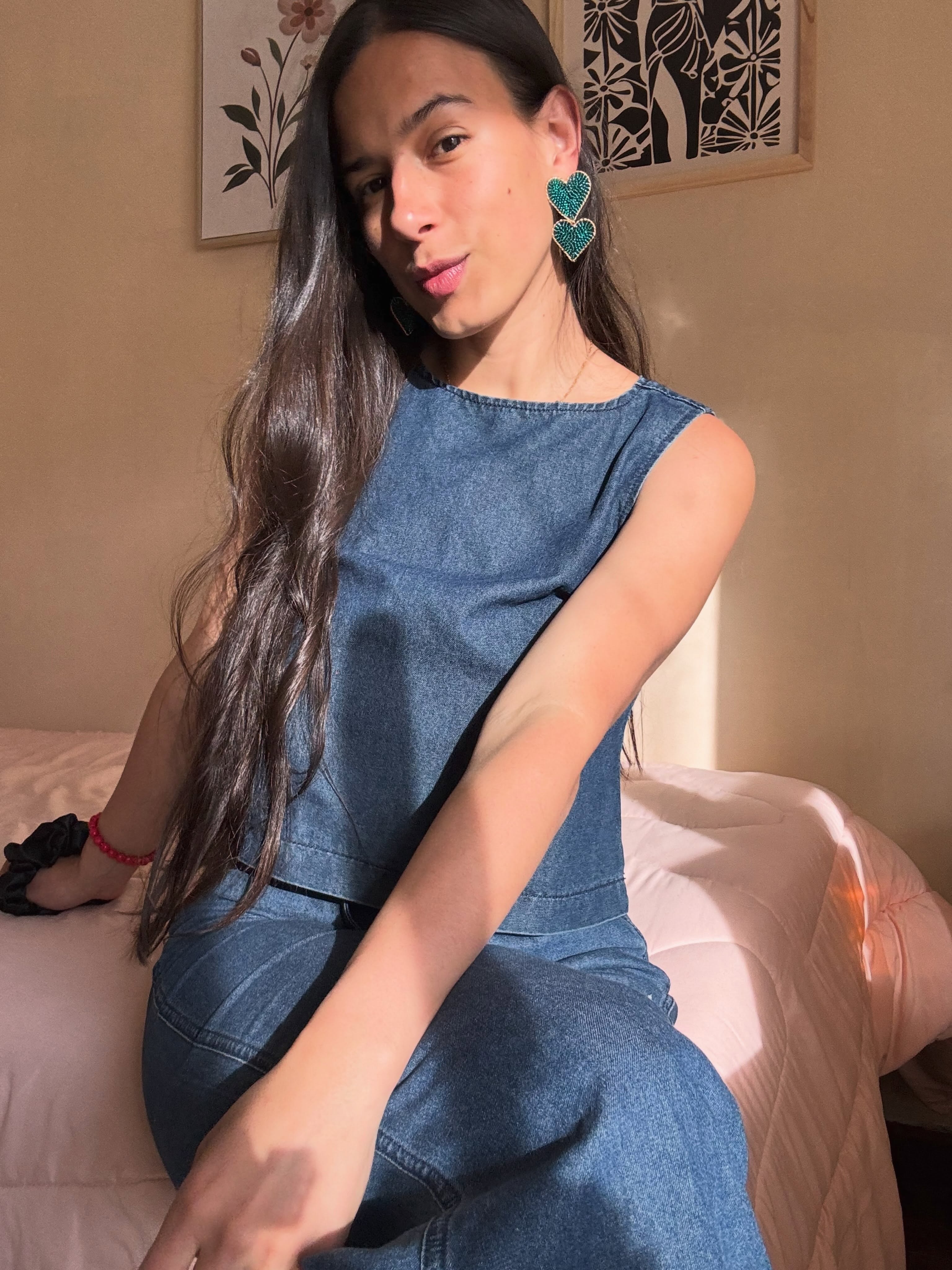 ohanna sitting on a bed wearing blue denim sleeveless top in bedroom
