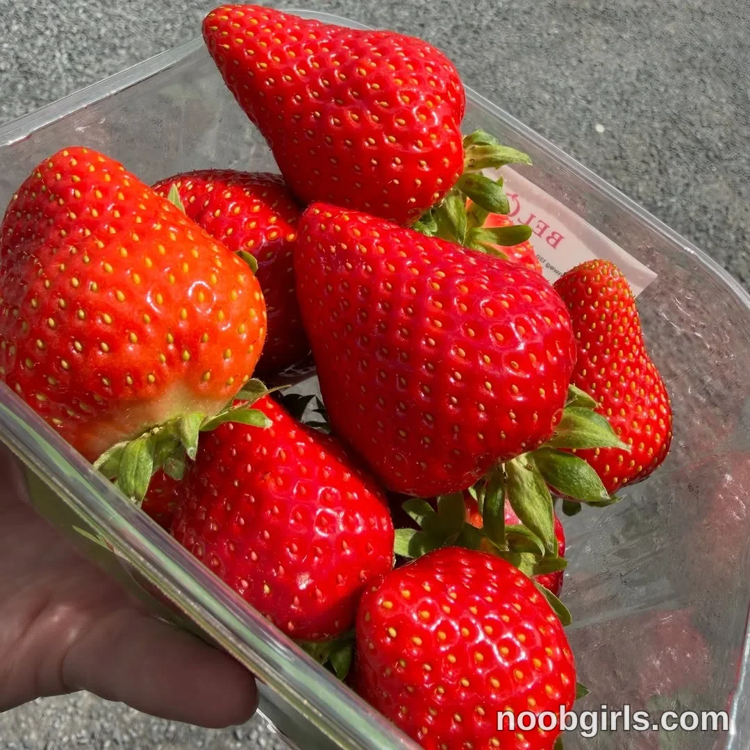Xena visible hand is holding the container of strawberries. in over a grey paved surface in Belgium, Europe