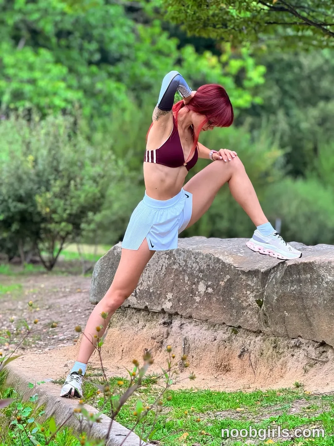 evaoopsy Standing with one foot on a large rock wearing Burgundy sports bra with three white stripes on one side