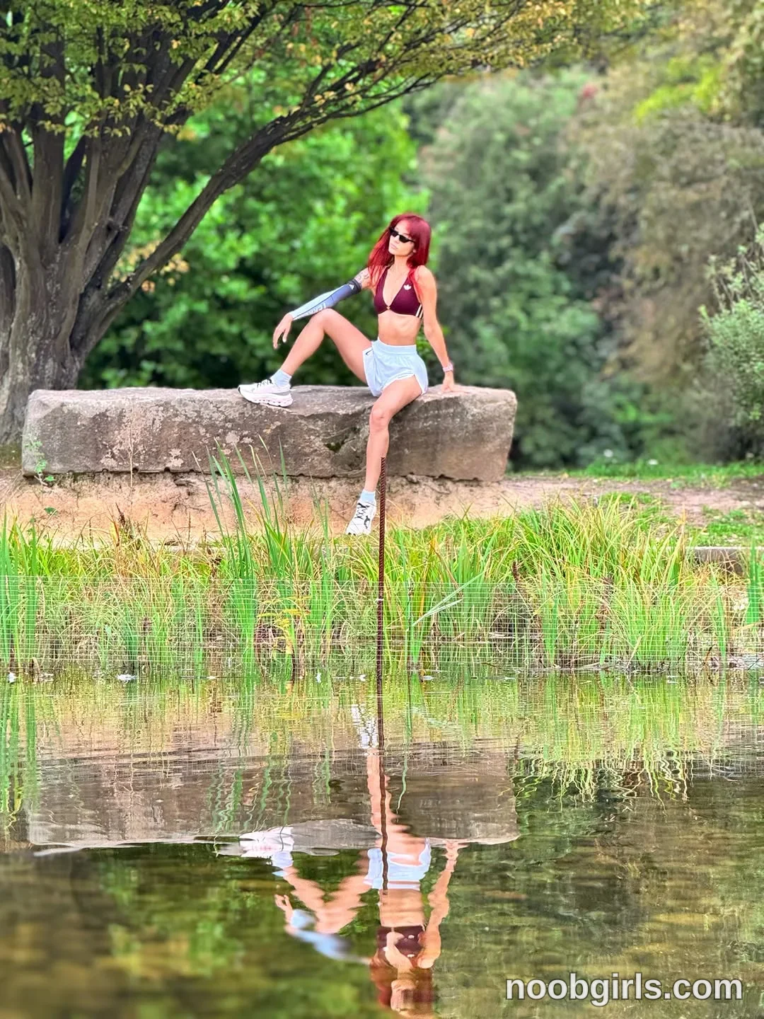 evaoopsy Sitting on a stone ledge with one knee raised wearing Burgundy bikini-style top beside a pond