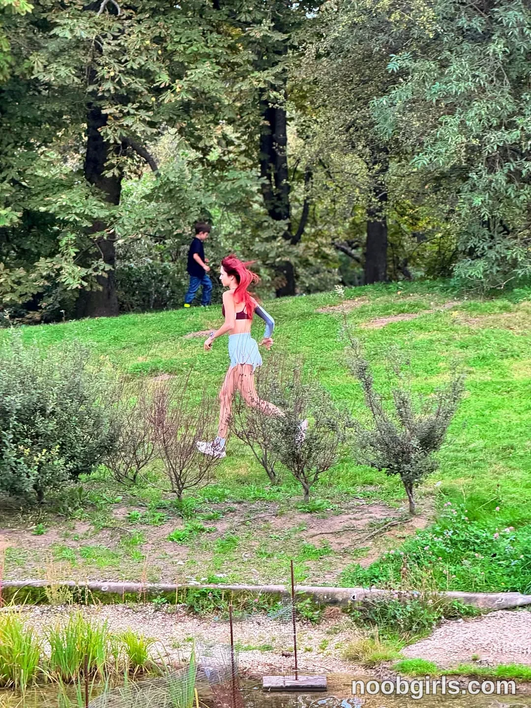 evaoopsy Walking across the grassy slope with her arms bent wearing Red cropped top with a dark band
