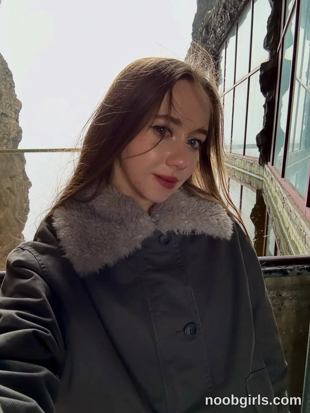 Elina taking a self-portrait photo wearing dark olive-grey buttoned coat with a grey faux-fur collar