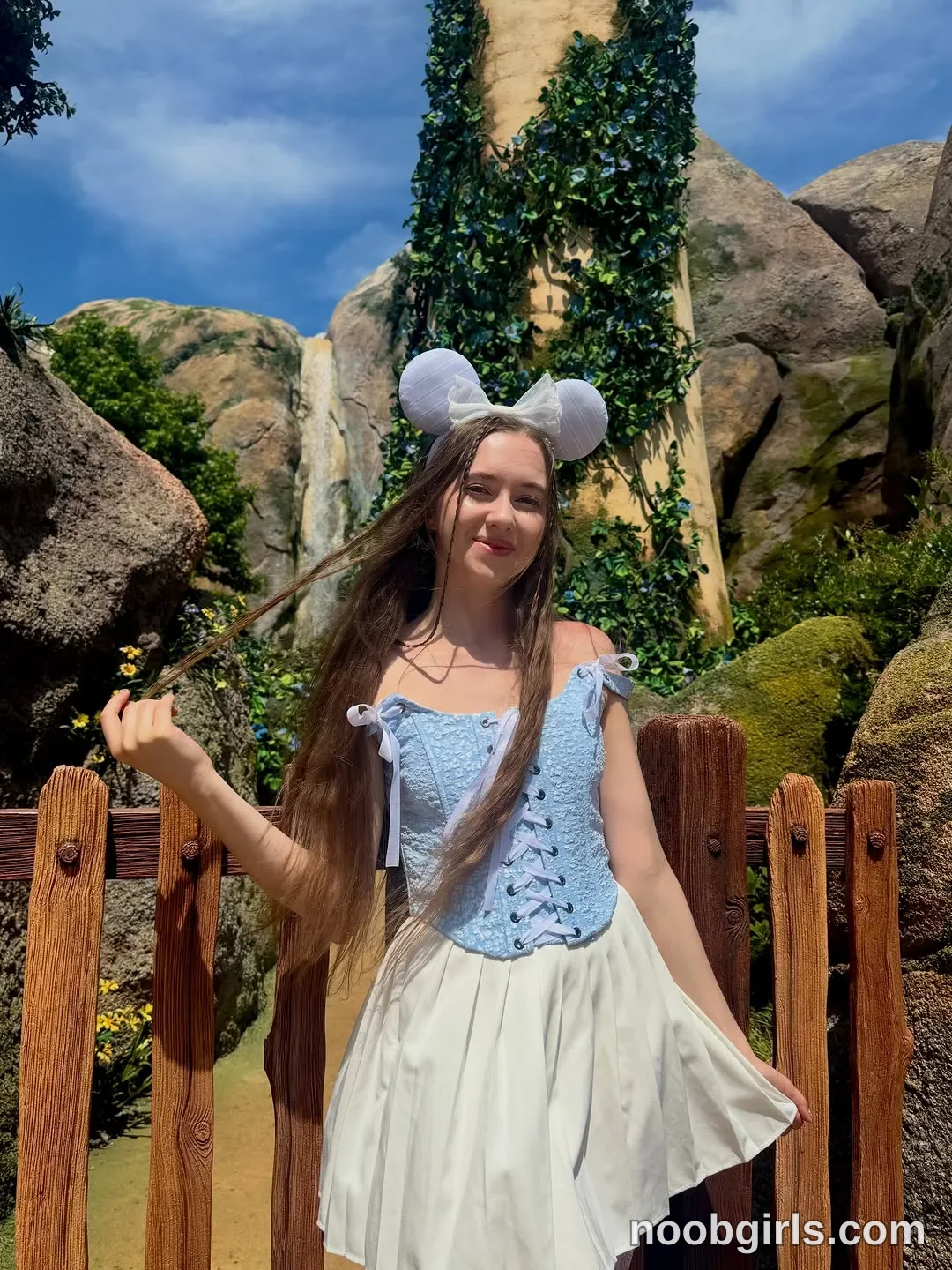 Elina standing outdoors by a fence wearing white mouse ears headband with a bow in theme park area in Tokyo DisneySea