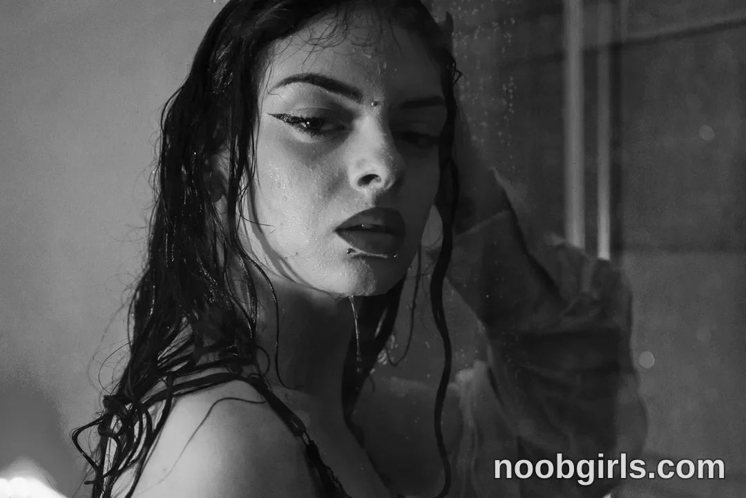Queen Pinky standing under falling water with wet hair wearing dark strappy garment or lingerie in shower stall or bathroom