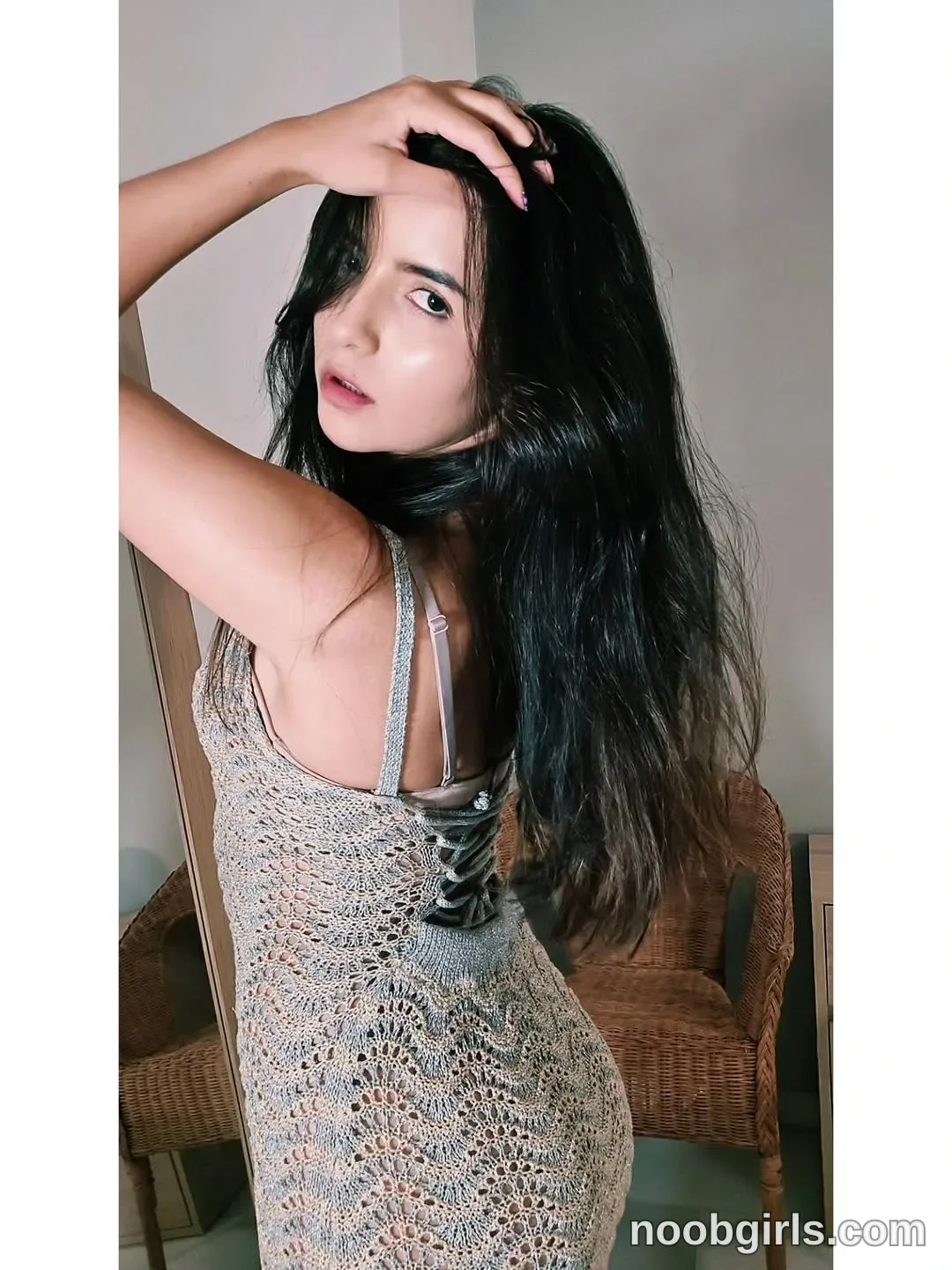 Raychell Black Standing with her back partly toward the camera wearing Grey open-knit sleeveless dress with narrow straps