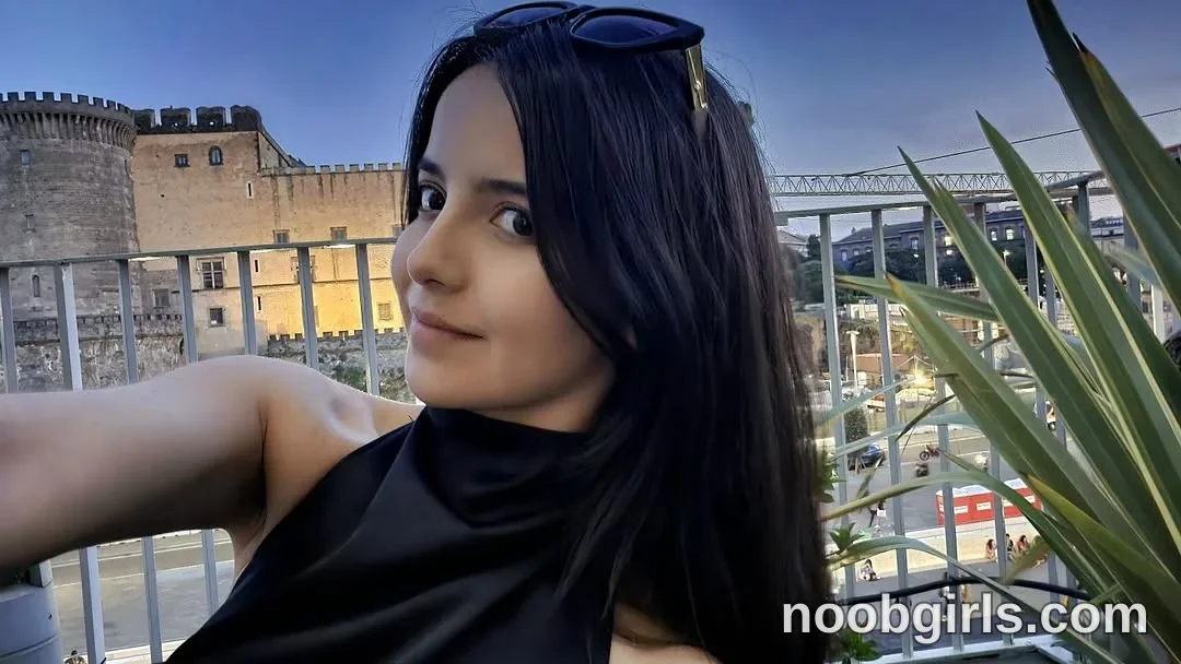 Raychell Black Extending one arm toward the camera with her head turned toward it wearing Black sleeveless high-neck top