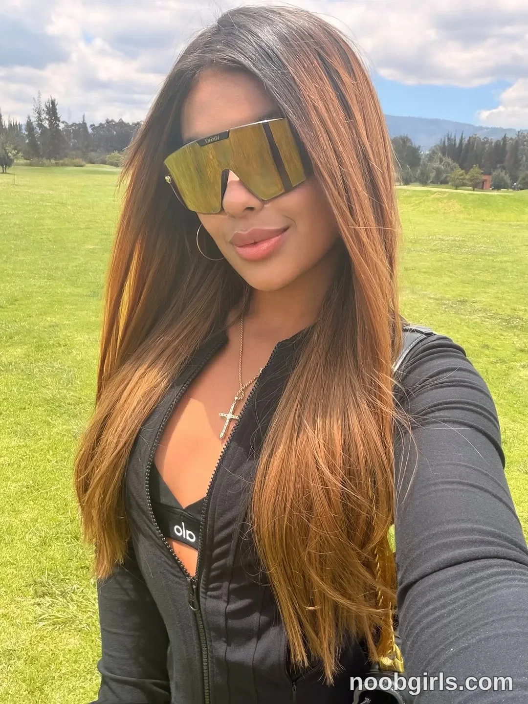 sary_hott taking a selfie wearing black long-sleeved zip-front jacket in open grassy field or golf course