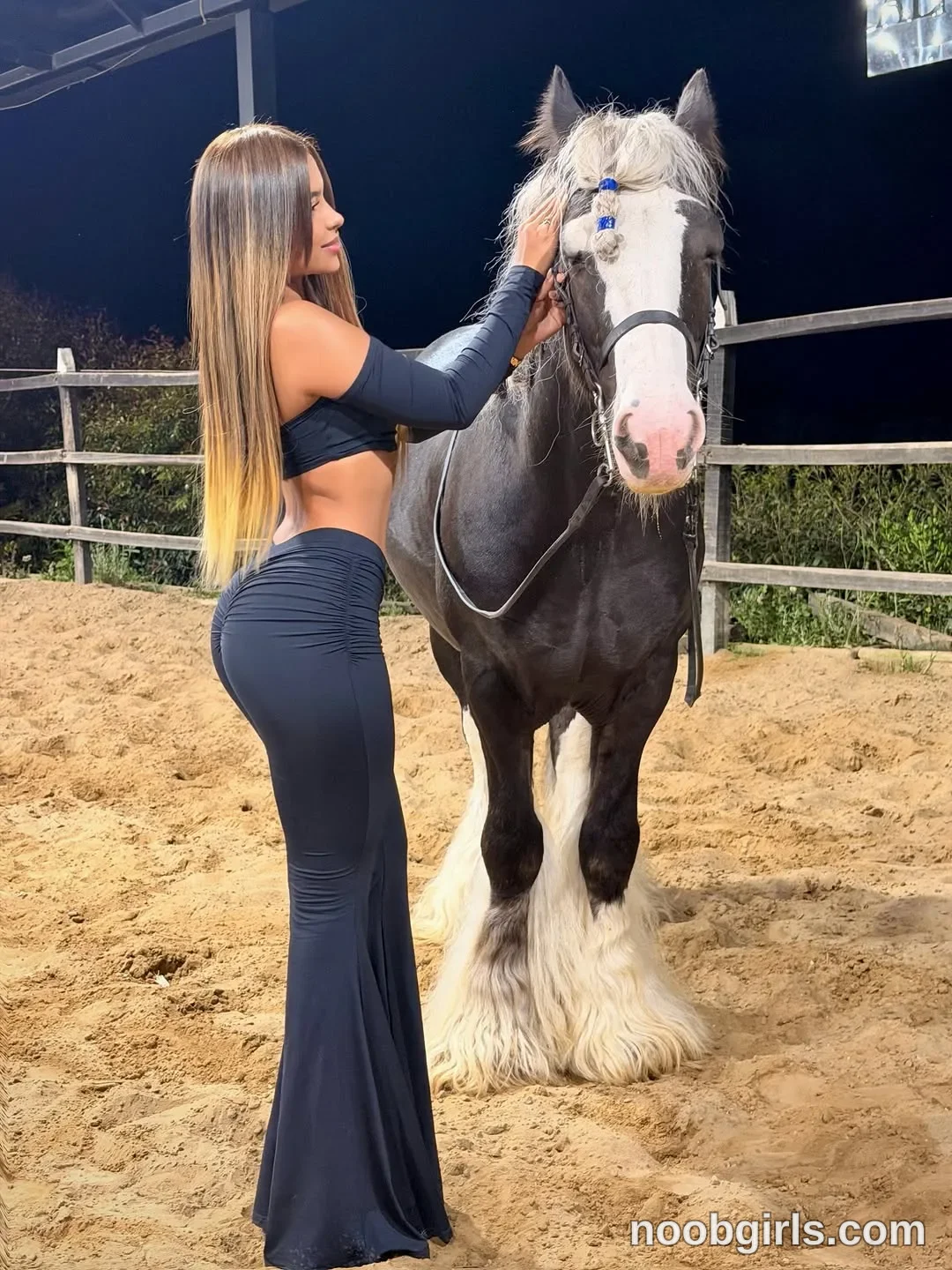 sary_hott standing next to a horse wearing black off-the-shoulder long-sleeve crop top in equestrian paddock or riding arena