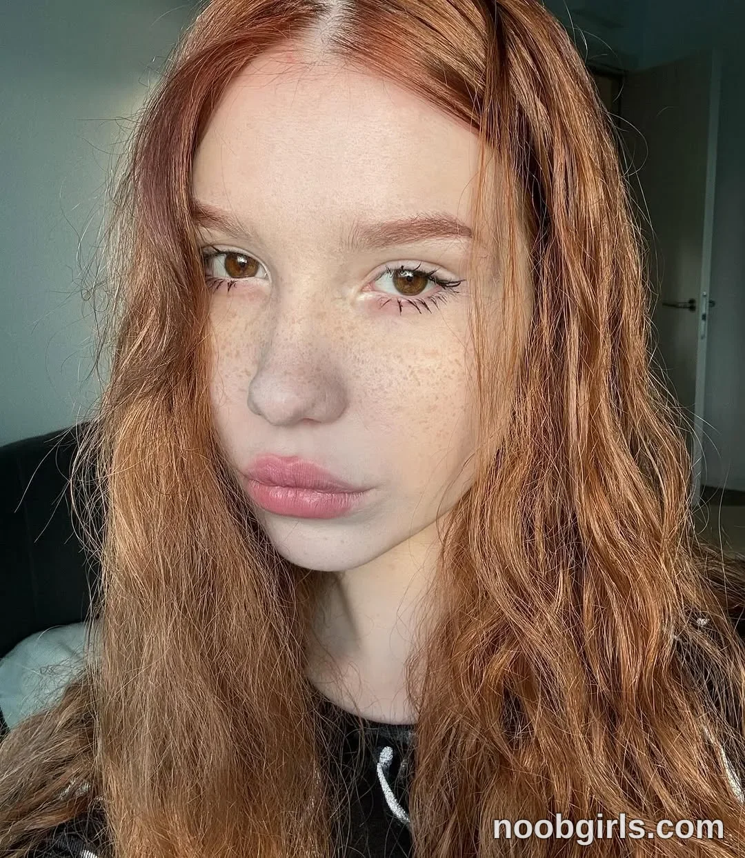 Jo Facing the camera with her head slightly turned wearing Black top with white drawstrings in room