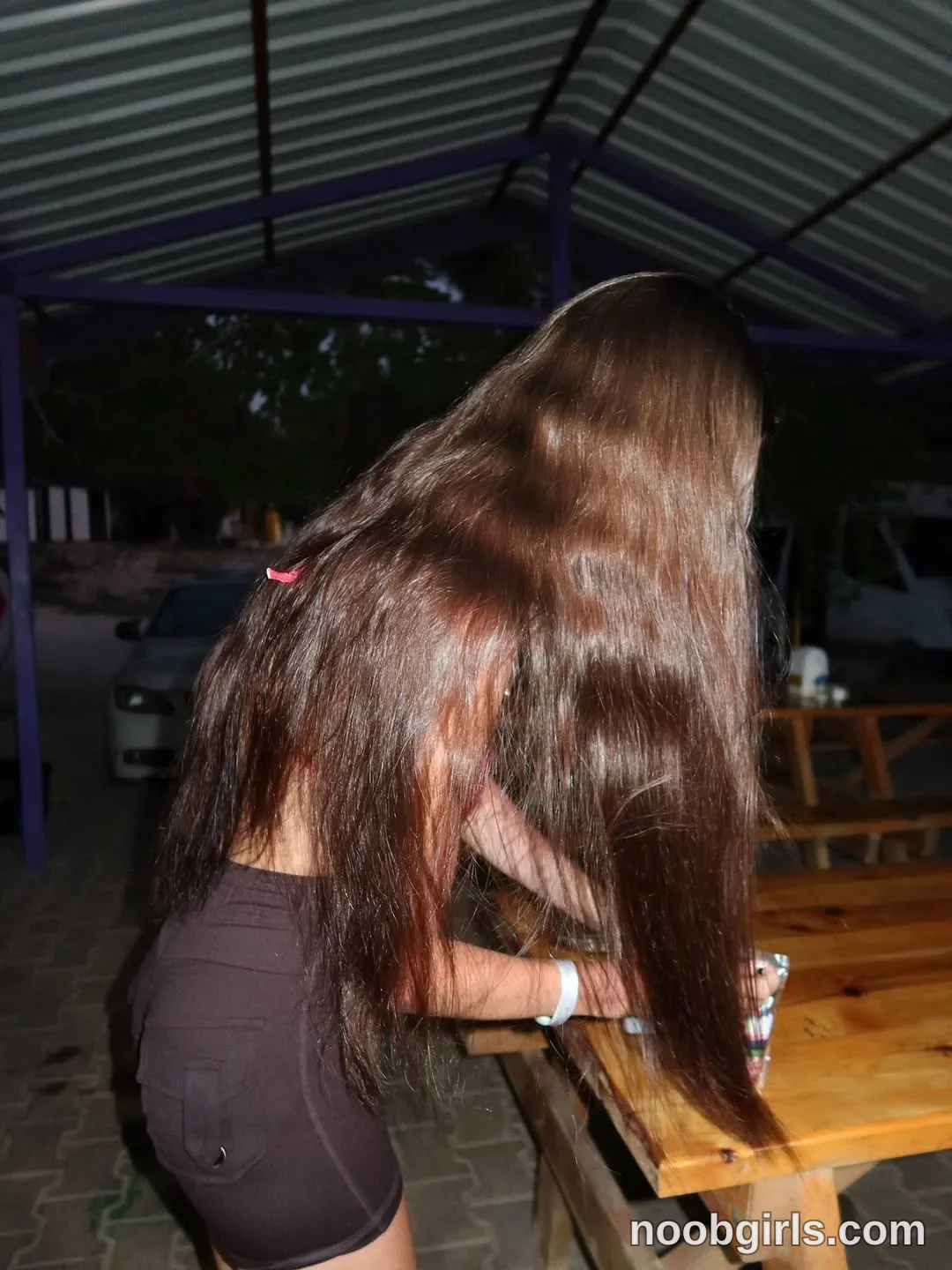 Maria Leaning forward beside a wooden table wearing Dark fitted shorts in covered seating area in Alanya